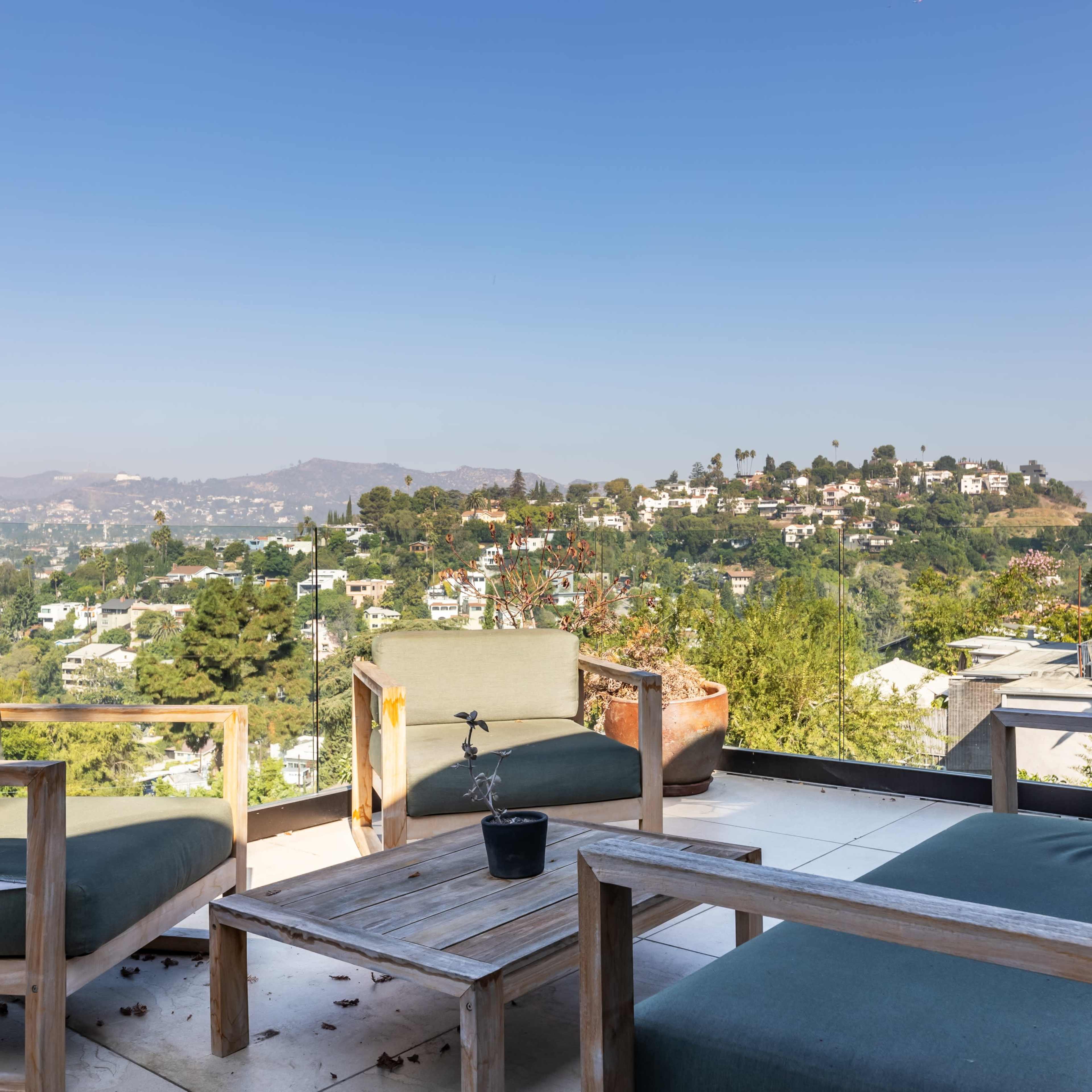 A patio with wooden furniture overlooks a hillside neighborhood under a clear blue sky.