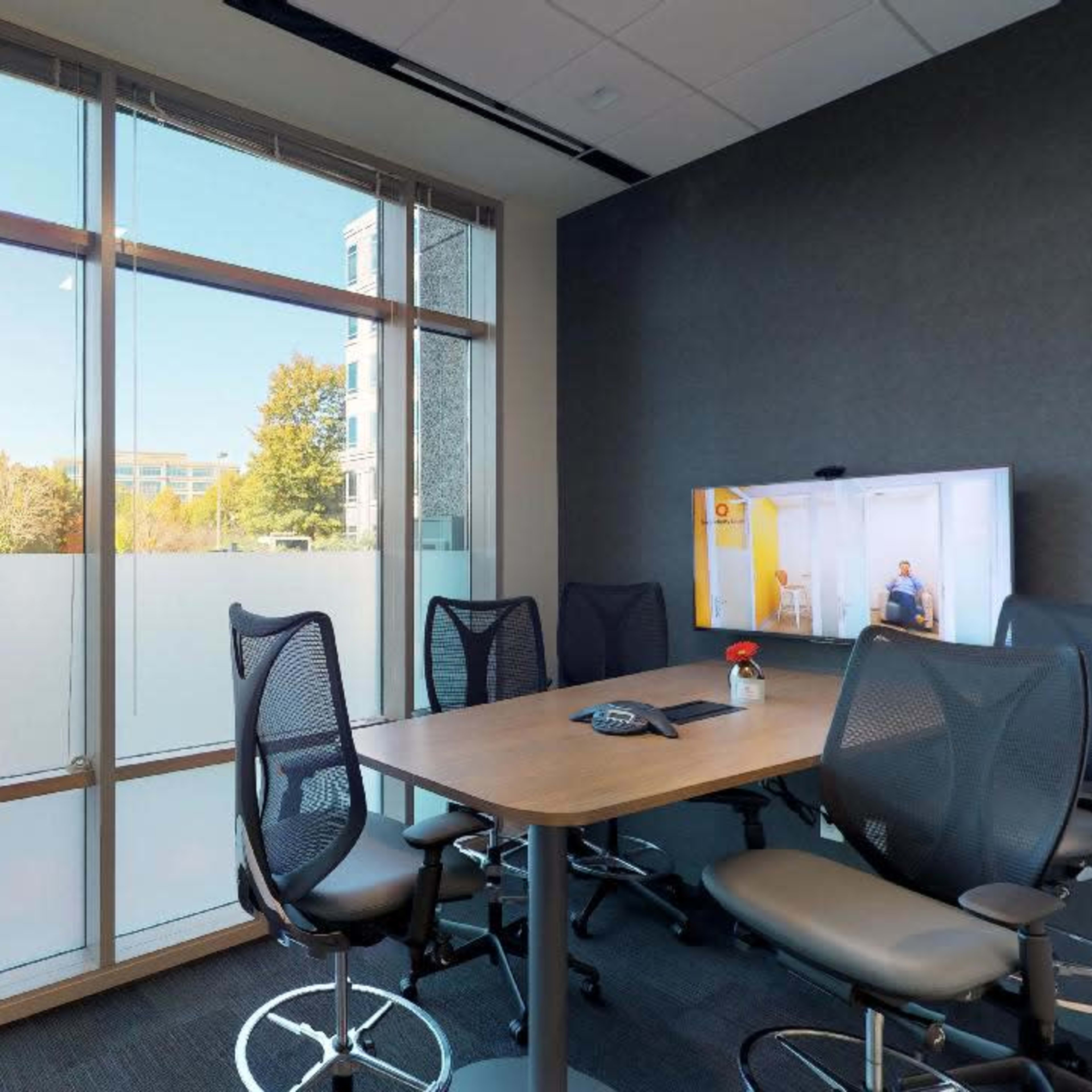 A modern conference room with a large window, a table, and several ergonomic chairs.