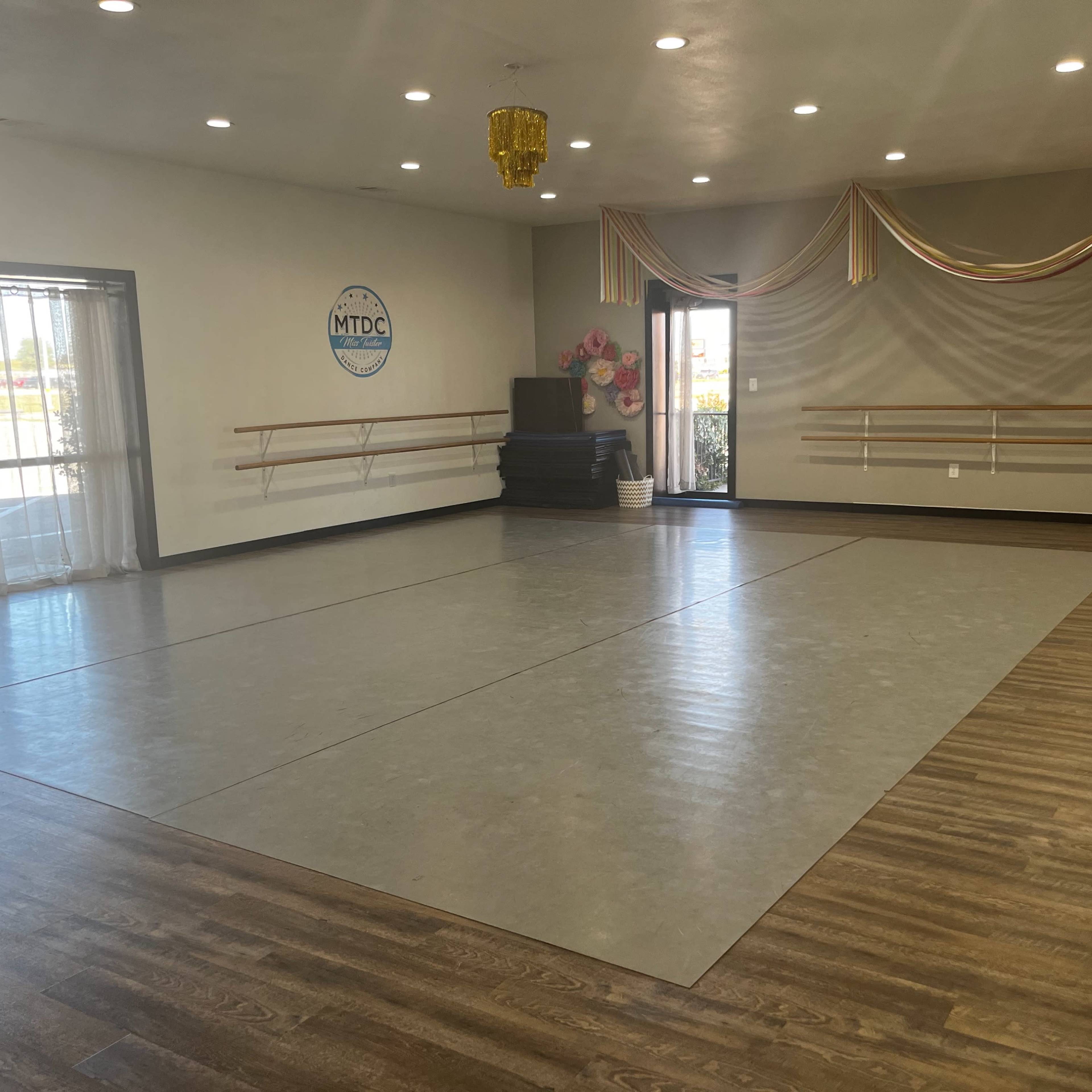 A spacious dance studio with a mirrored wall, ballet barres, and a decorated entrance.