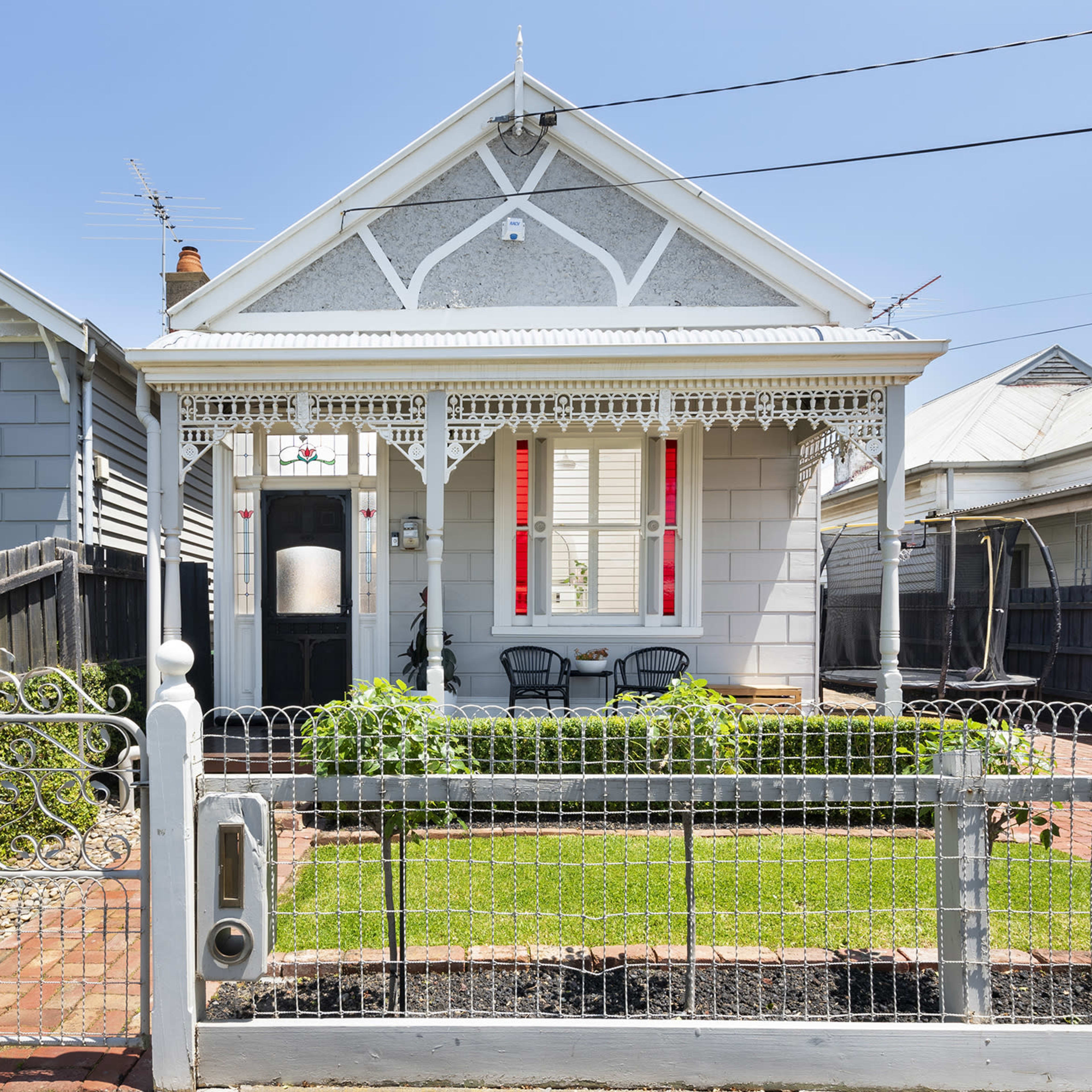 A vintage-style house with a decorative fence, a well-kept front garden, and a porch with two chairs.