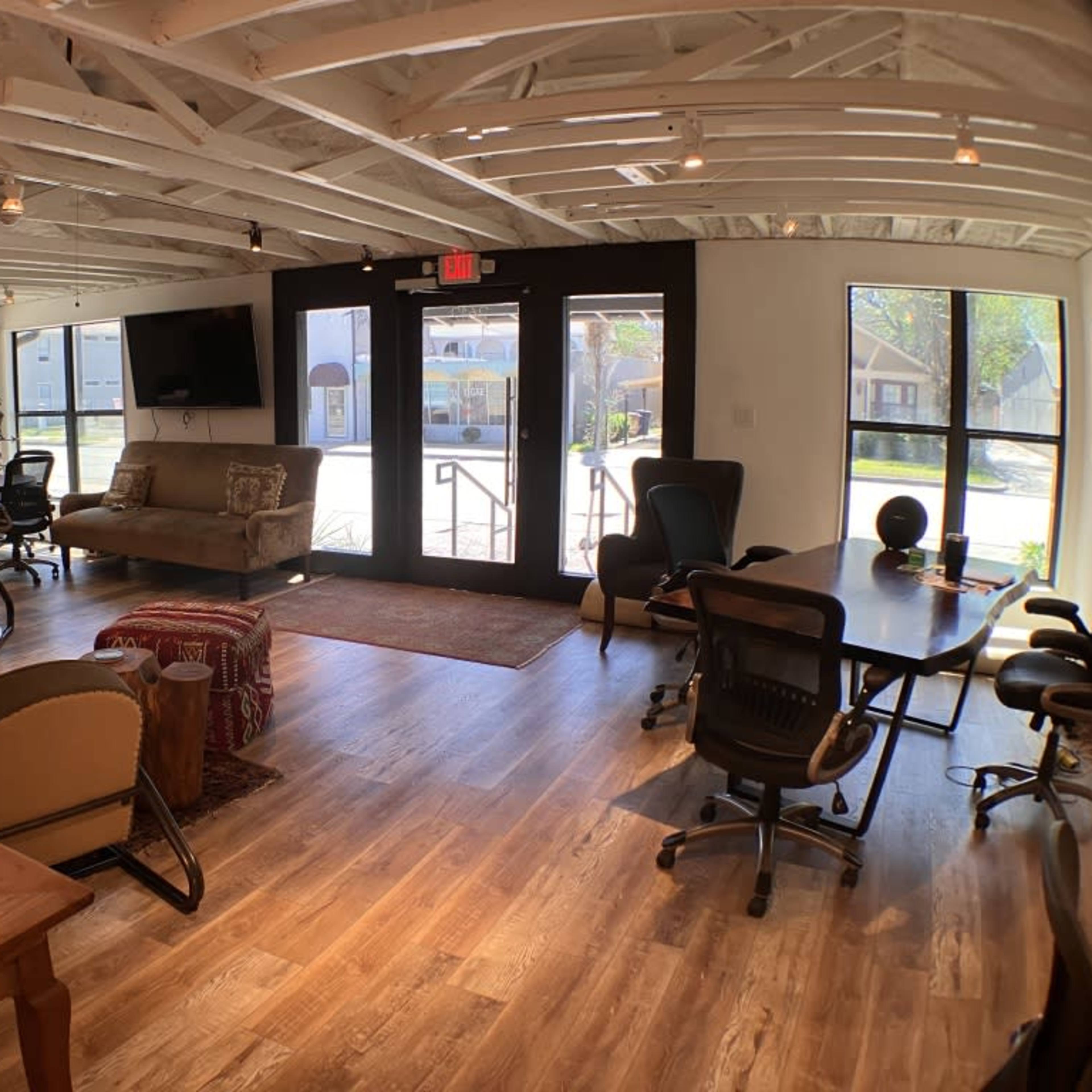 A spacious office with wooden floors, a mix of seating areas, and large windows allowing natural light to enter.