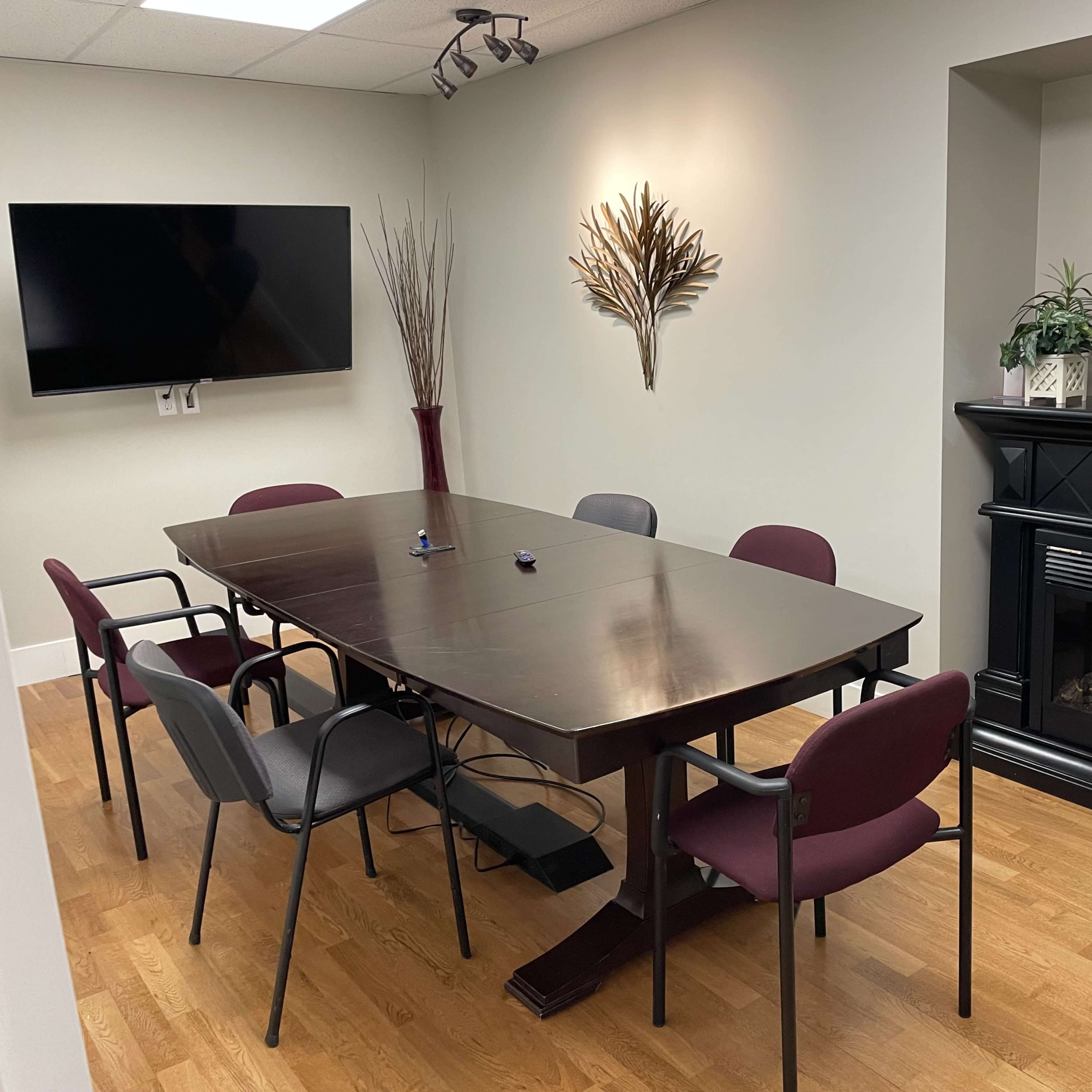A conference room features a large table surrounded by chairs, a wall-mounted television, and a decorative fireplace.