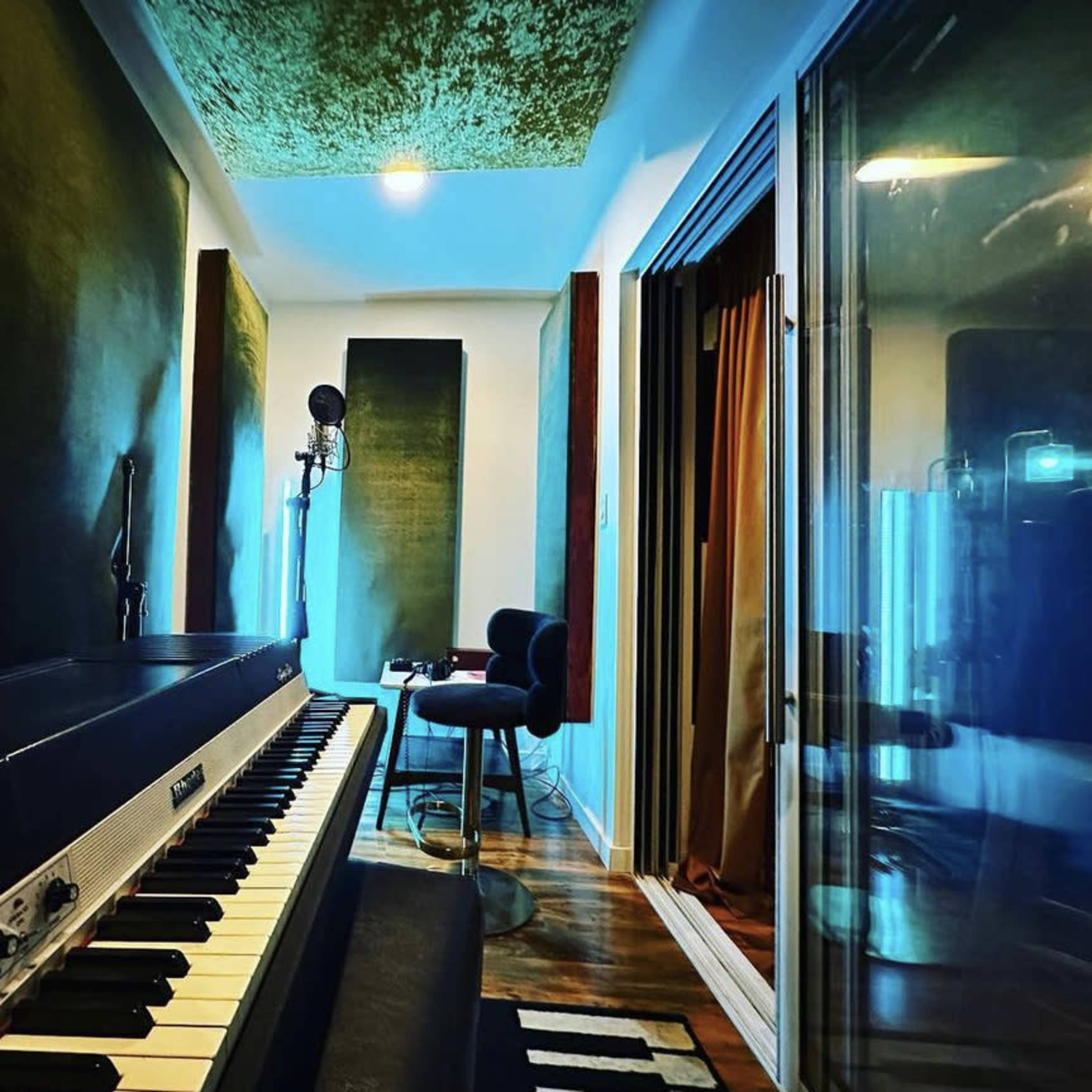 A music studio with a piano, microphone, and soundproof walls, illuminated by soft lighting.