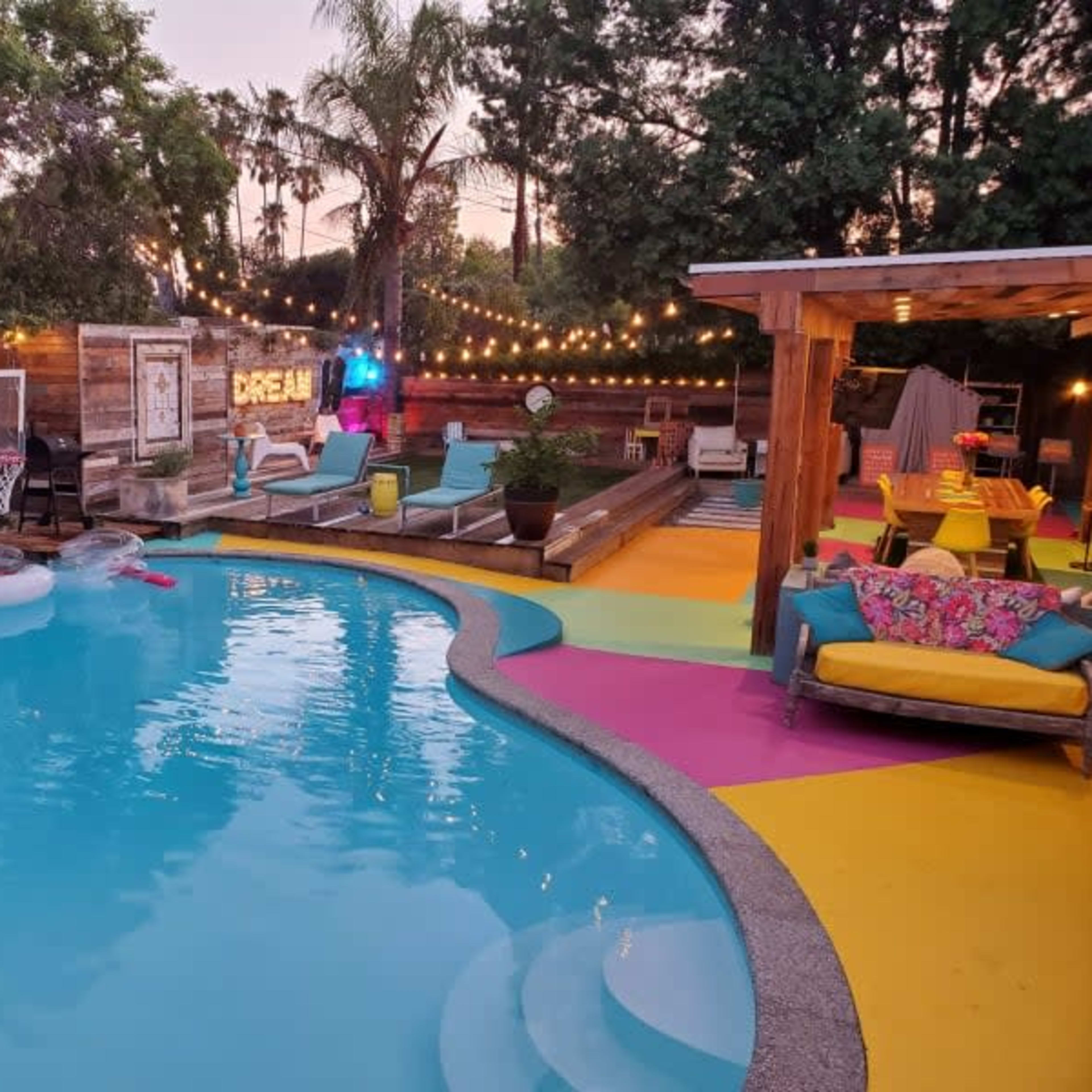 A colorful backyard featuring a swimming pool, lounge chairs, and string lights illuminating the area.