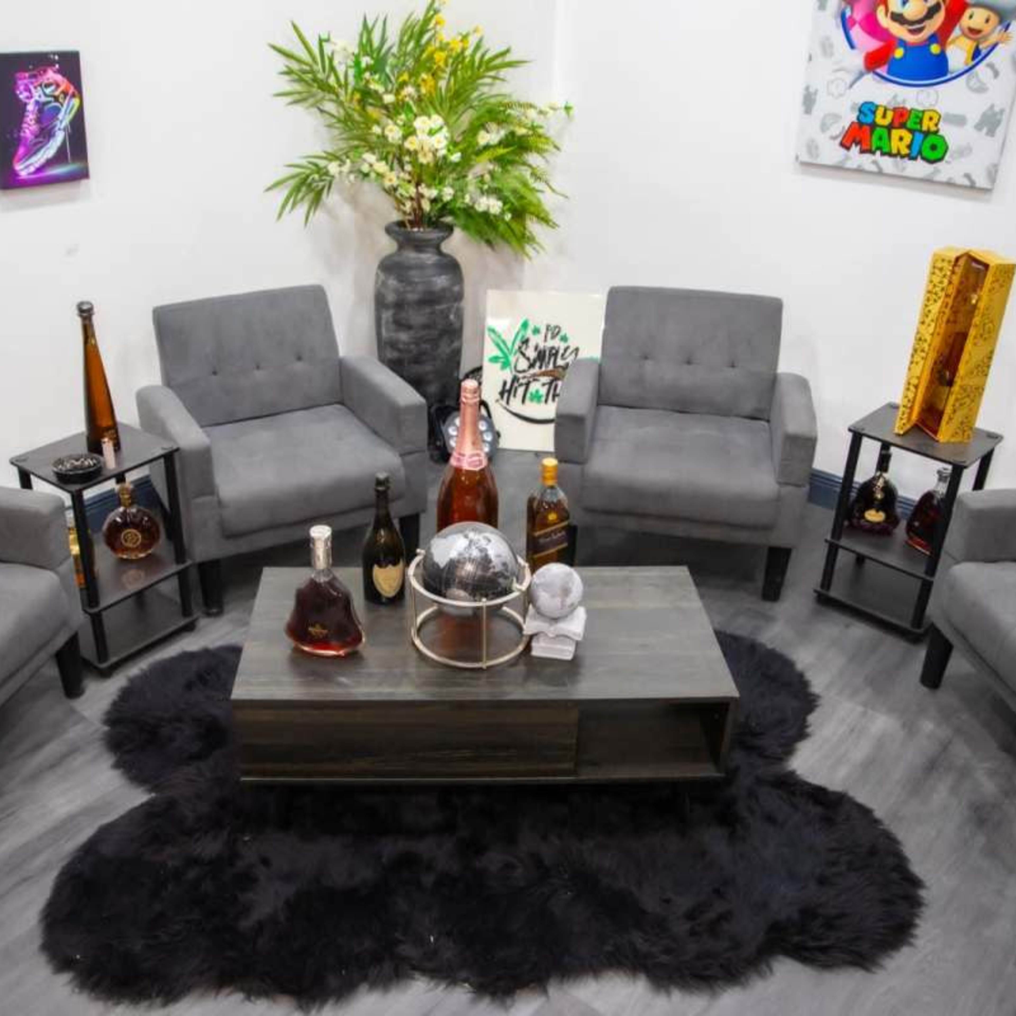 A modern seating area with gray chairs arranged around a coffee table, complemented by decorative bottles on stands and a fur rug.