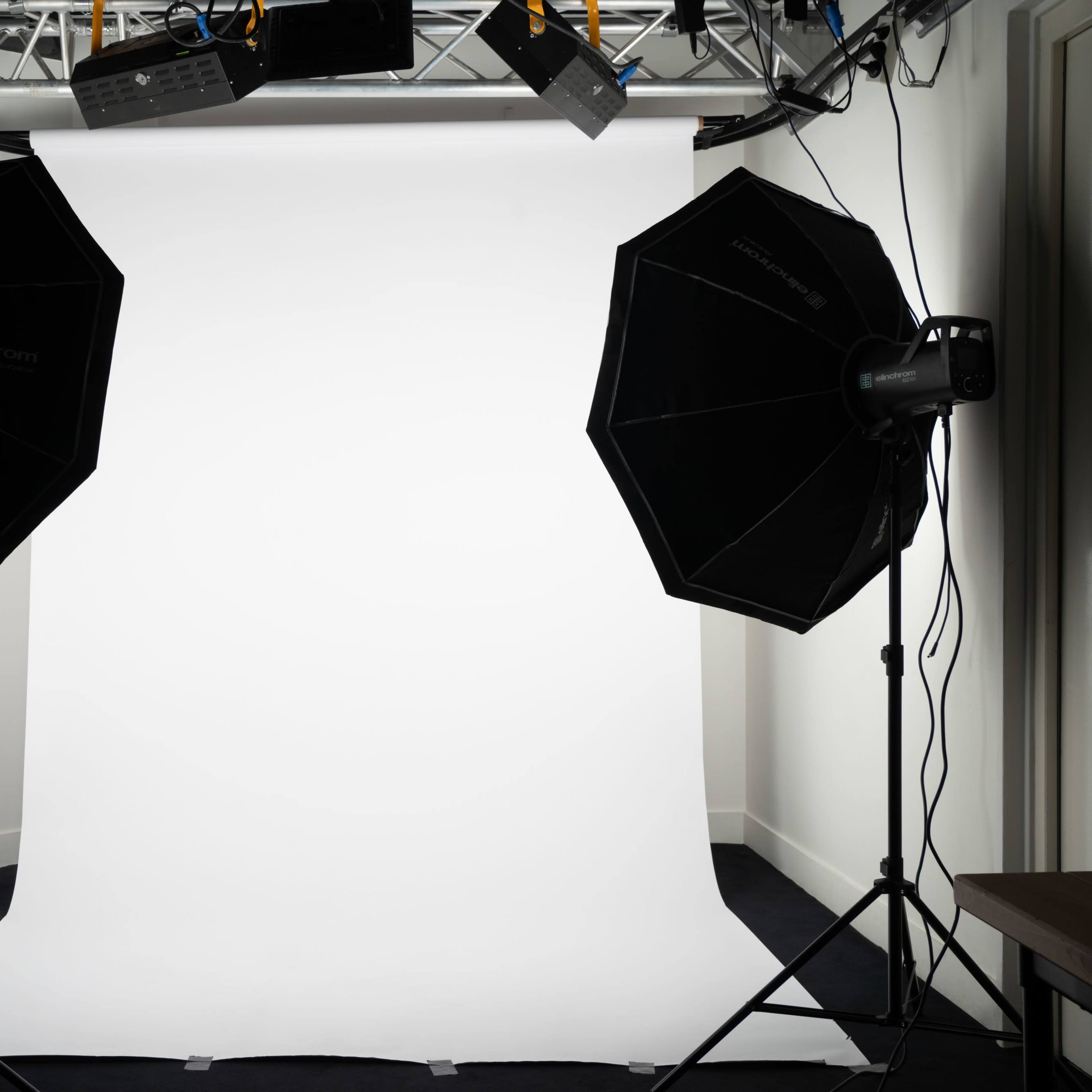 A photography studio setup with two large softbox lights flanking a white backdrop.