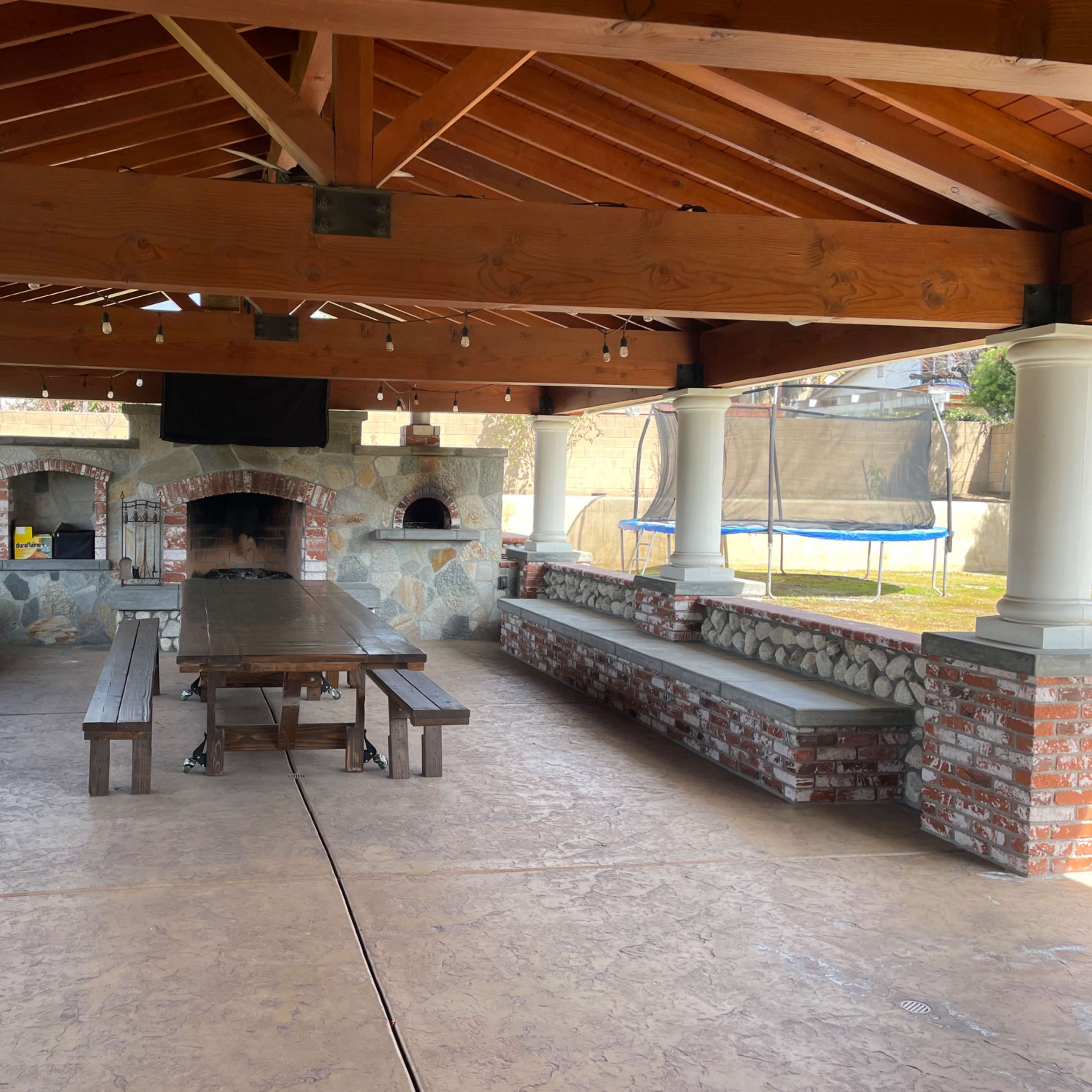 A spacious outdoor pavilion with a brick oven and seating areas made of stone and wood.