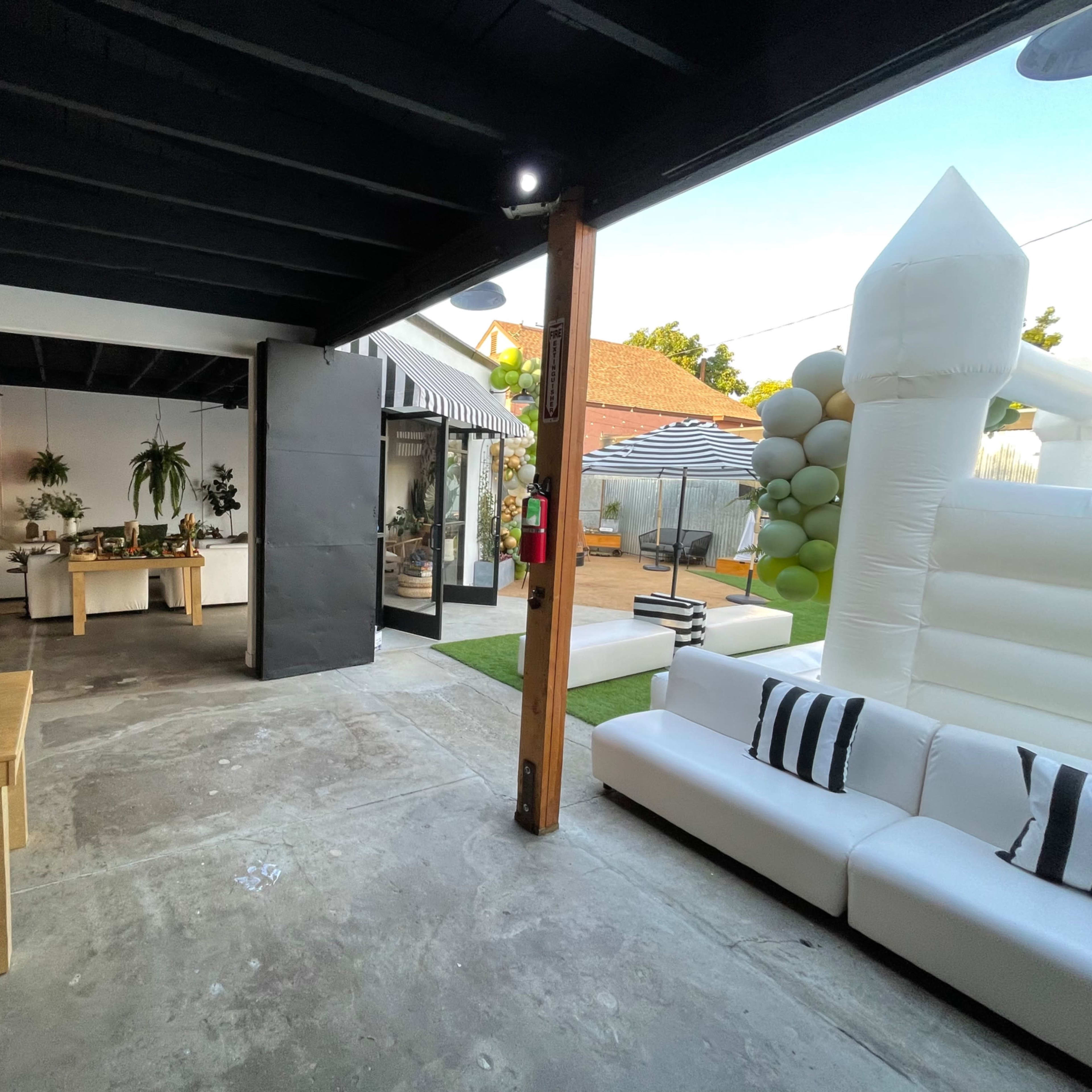 A spacious, modern indoor and outdoor area featuring a white sofa, a wooden table, and a large inflatable bounce house in the backyard.