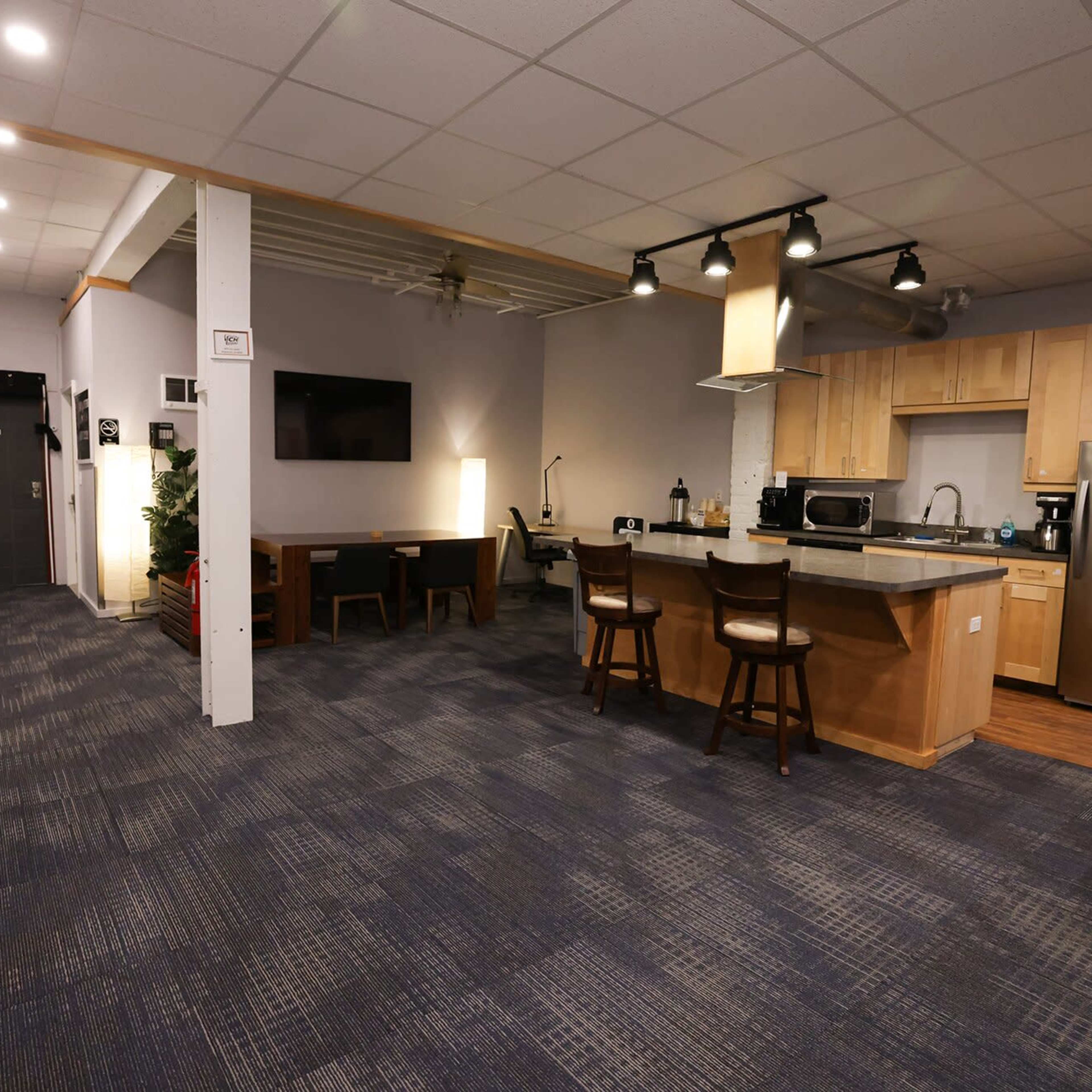 A modern kitchen and dining area with wood cabinetry, a countertop, and a small table with chairs, adjacent to a hallway.