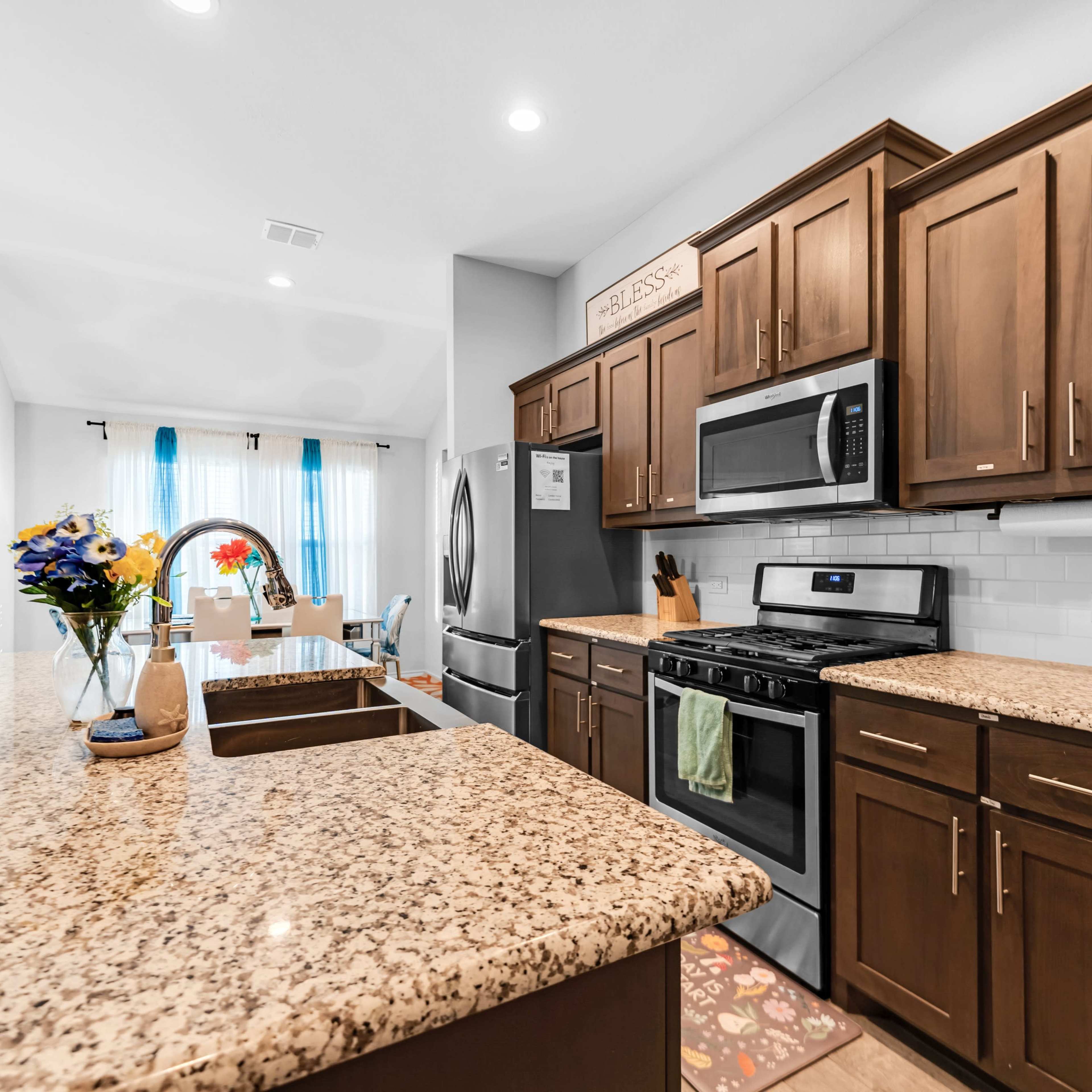 The kitchen features dark wooden cabinets, stainless steel appliances, and a granite countertop with a decorative island and a vase of flowers.