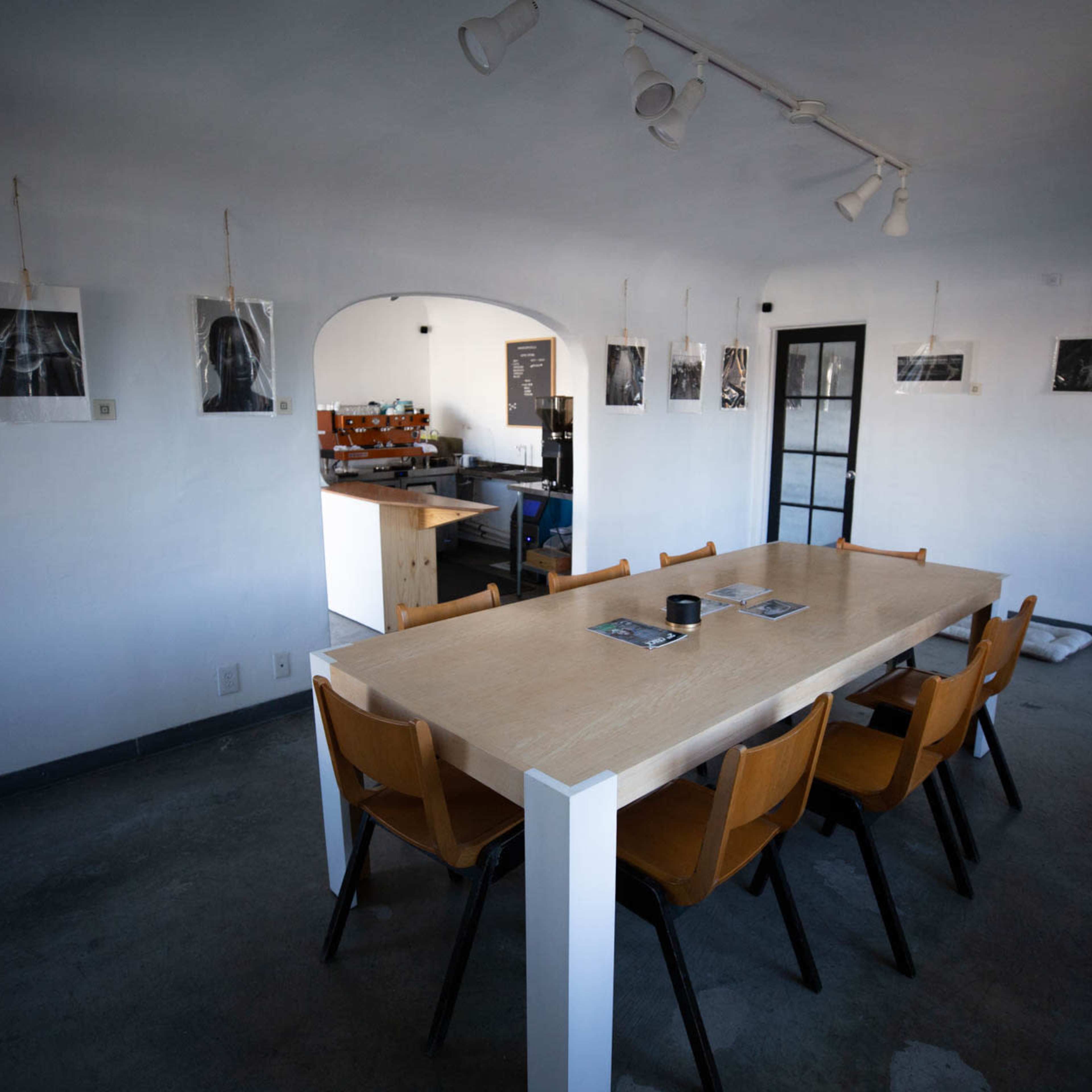 A long wooden table with eight chairs is positioned in a minimalist room featuring black and white photographs hung on the walls.