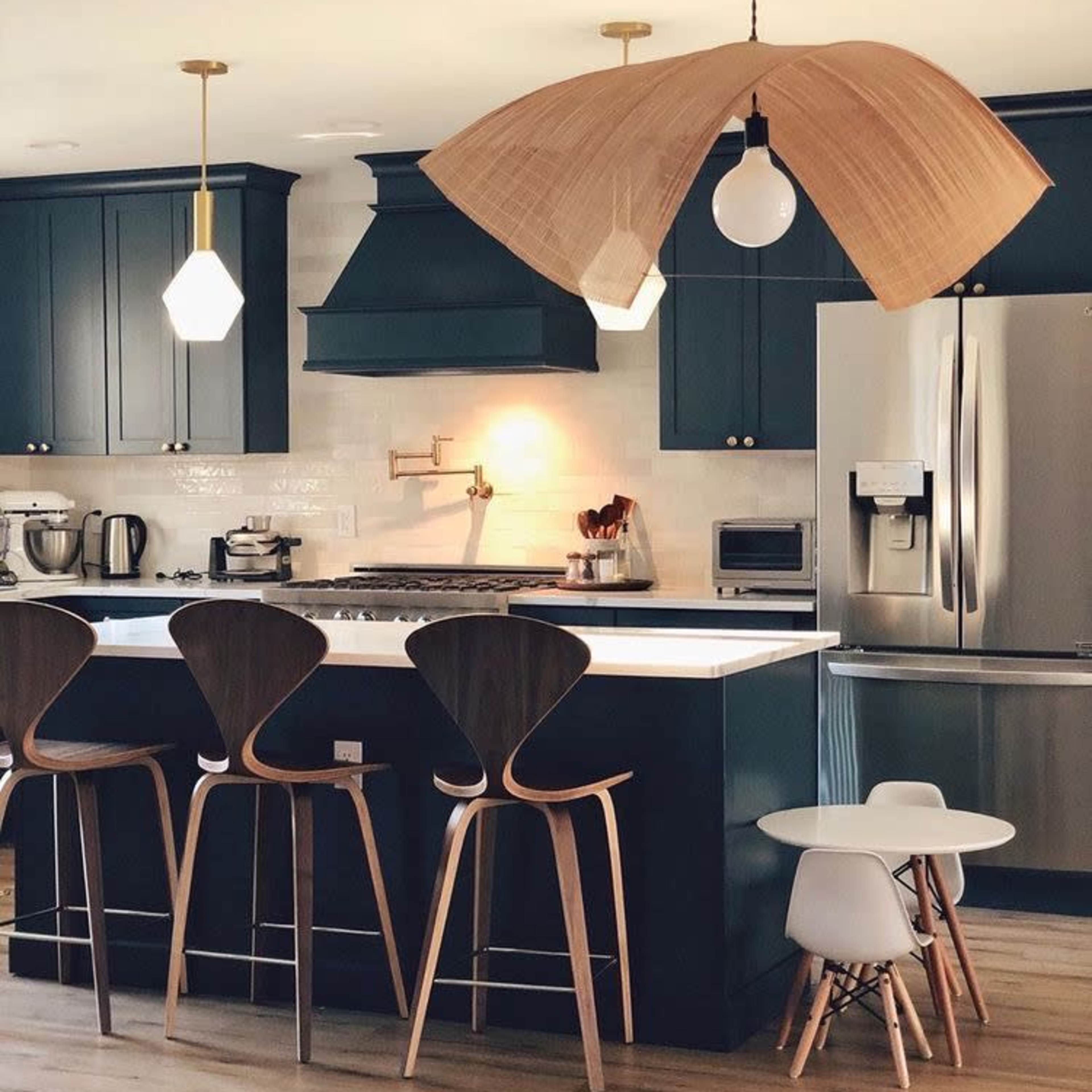 A modern kitchen features dark blue cabinets, a large refrigerator, and a unique pendant light above a breakfast bar with wooden stools.