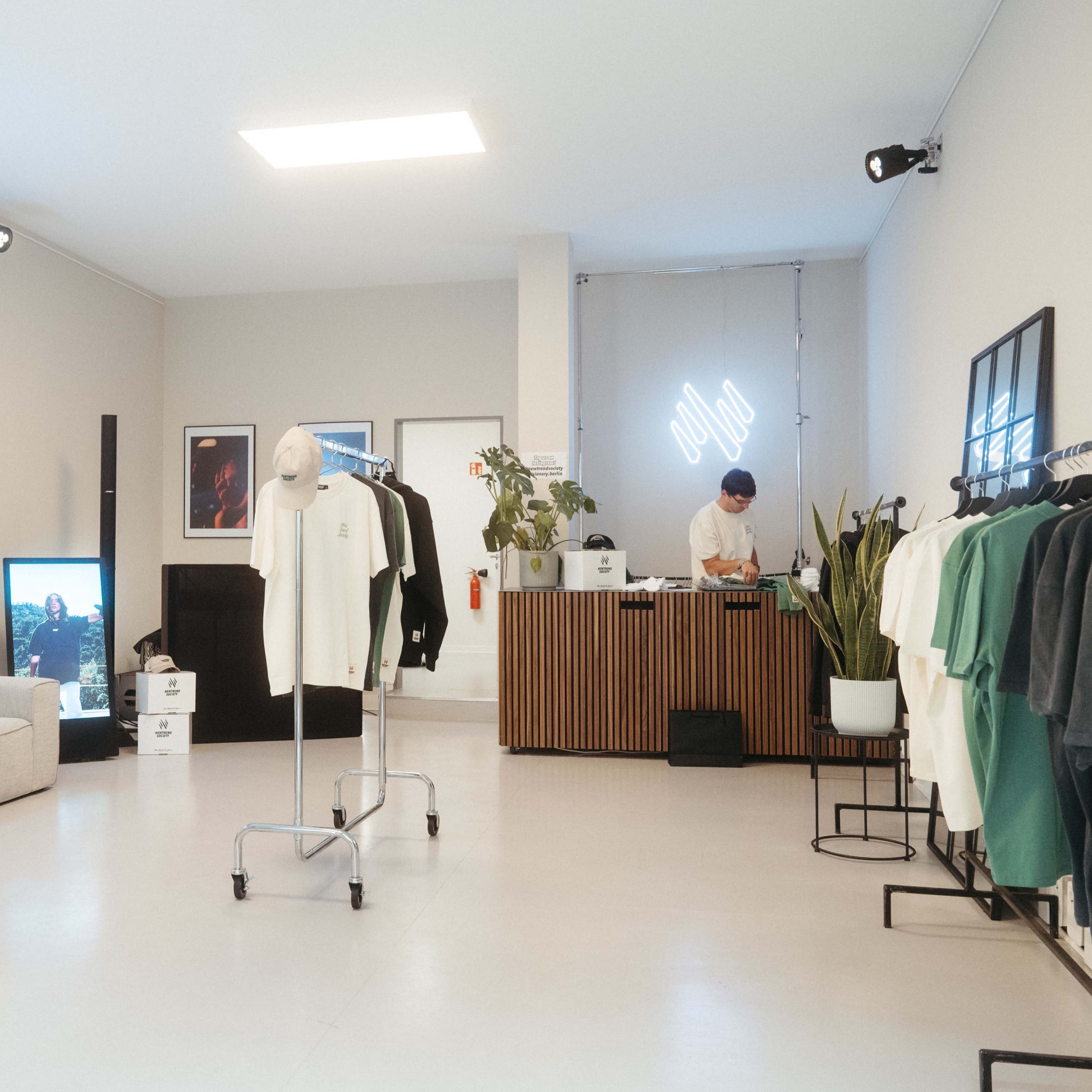A modern retail space featuring clothing racks, a reception desk, a display screen, and a gray sofa.