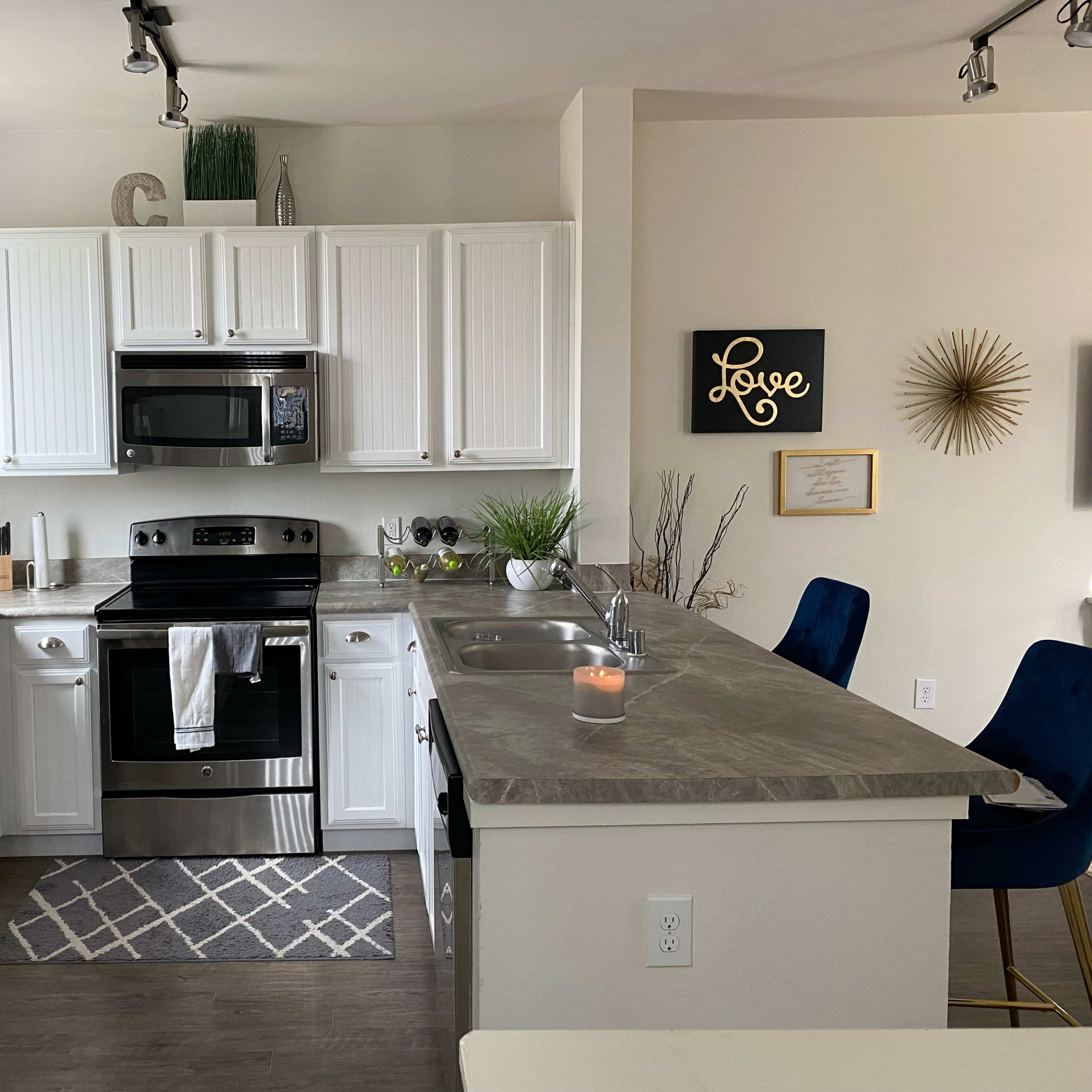 A modern kitchen with white cabinets, stainless steel appliances, and a central island featuring bar stools.