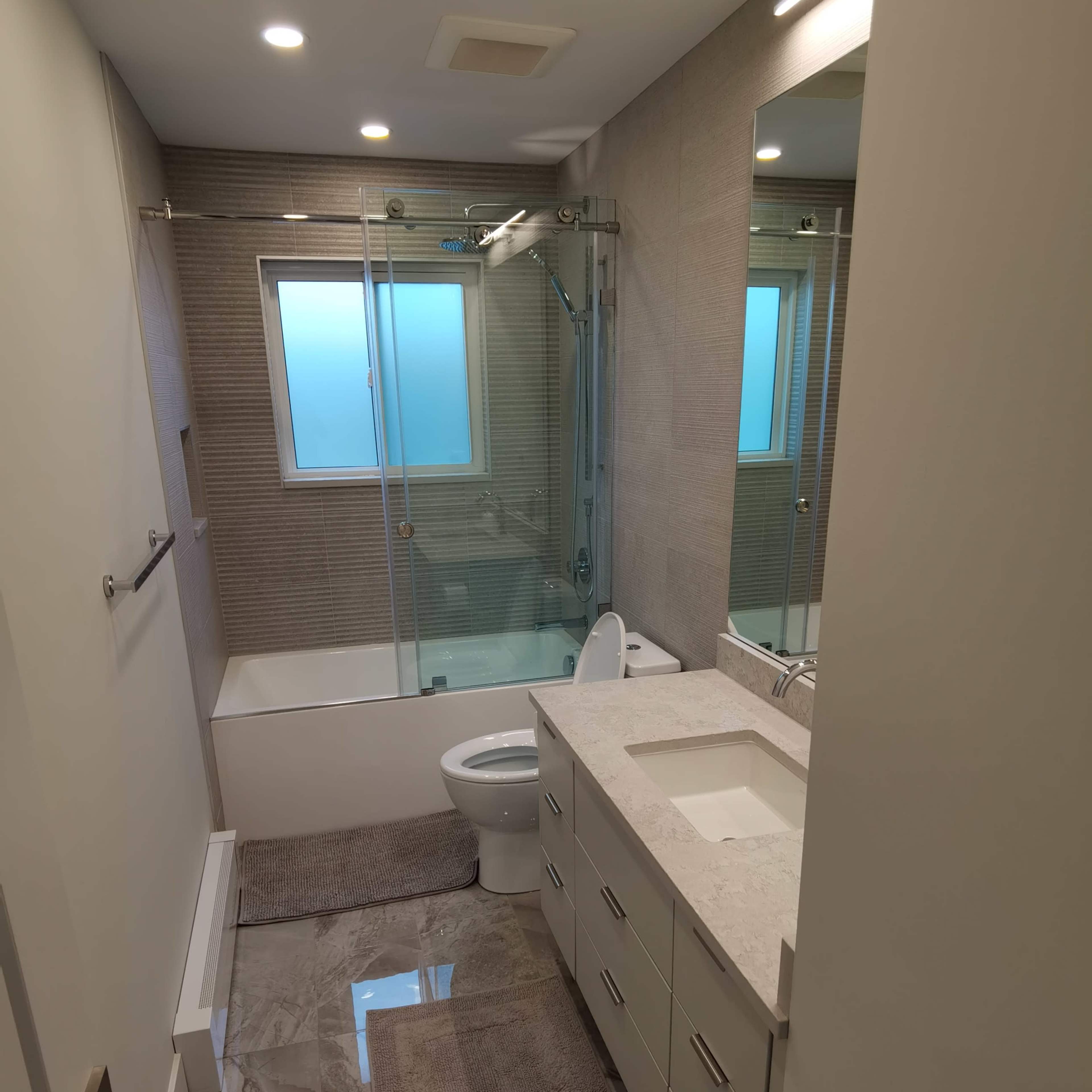 A modern bathroom featuring a glass shower, a bathtub, a toilet, and a double sink vanity with a countertop.