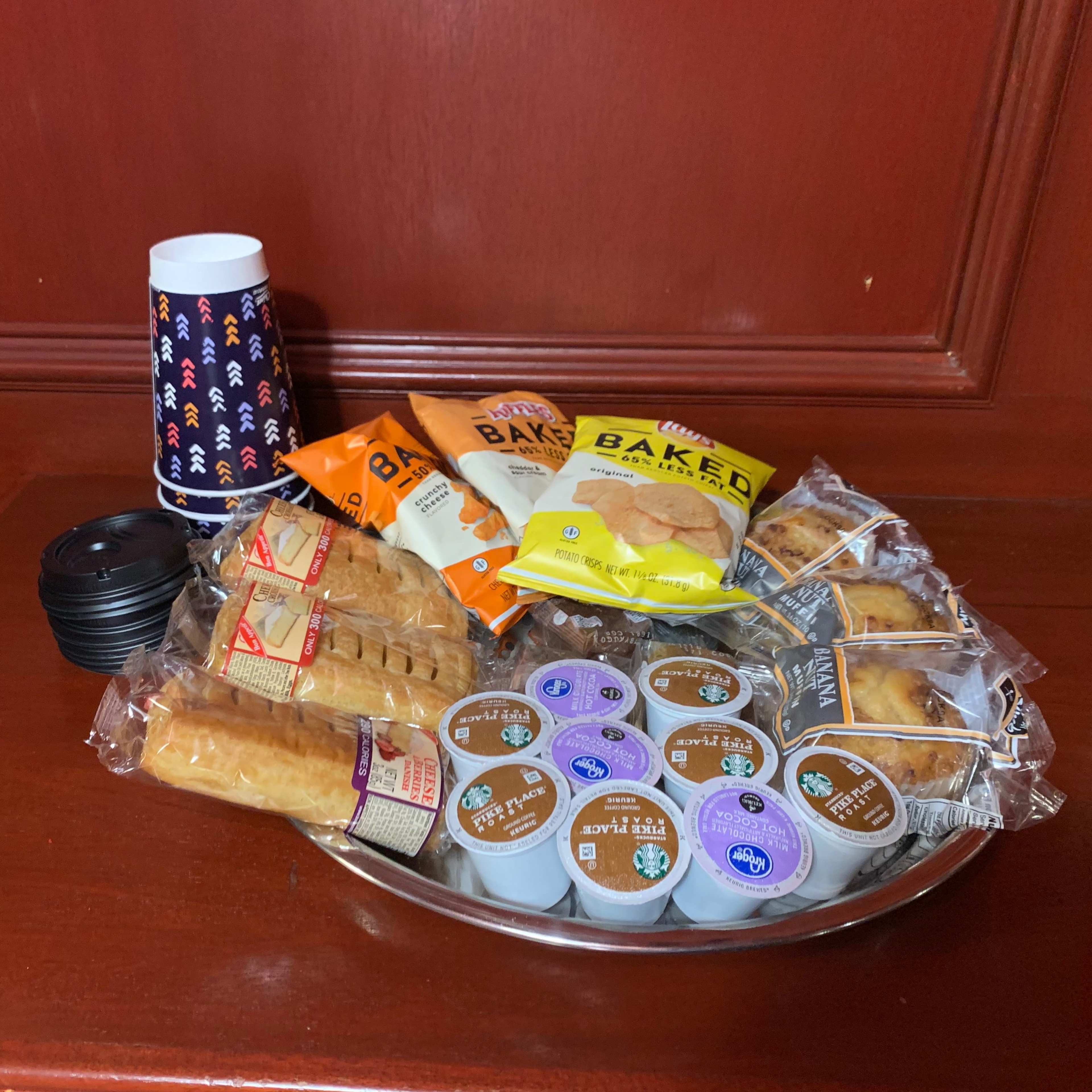A platter of assorted baked goods, including cookies and pastries, accompanied by cups and condiments, is arranged on a wooden surface.