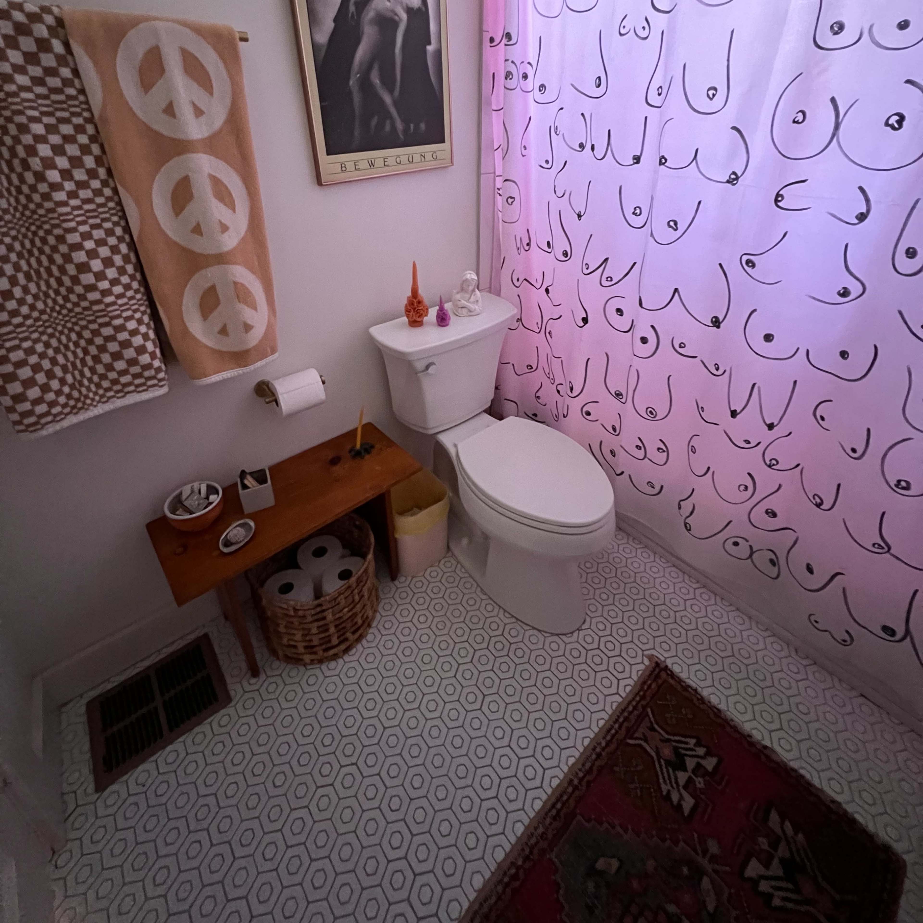 A small bathroom featuring a toilet, a patterned shower curtain, a towel with a peace symbol, and decorative elements on the walls and floor.