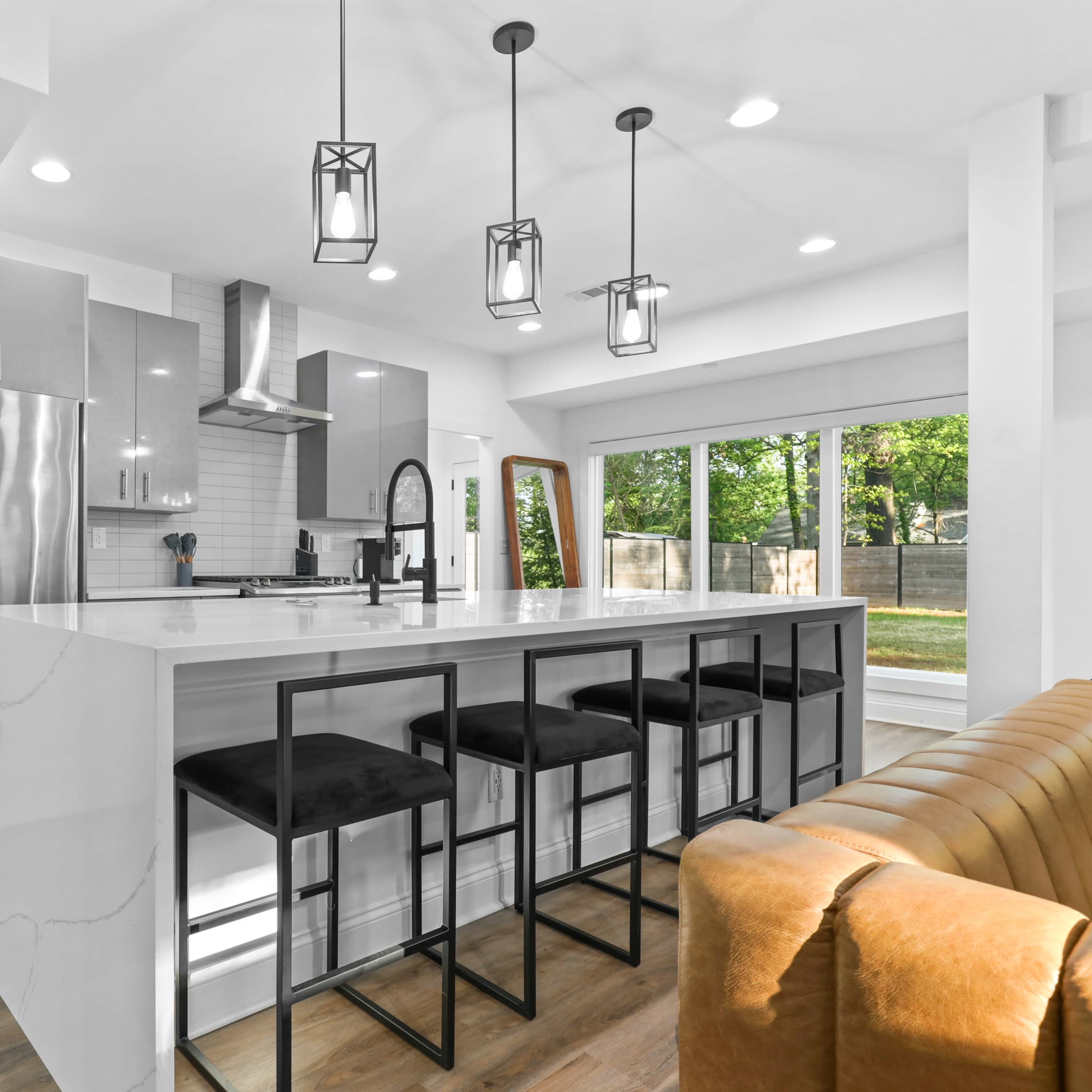 The modern kitchen features sleek gray cabinetry, stainless steel appliances, and a large white island with black bar stools.