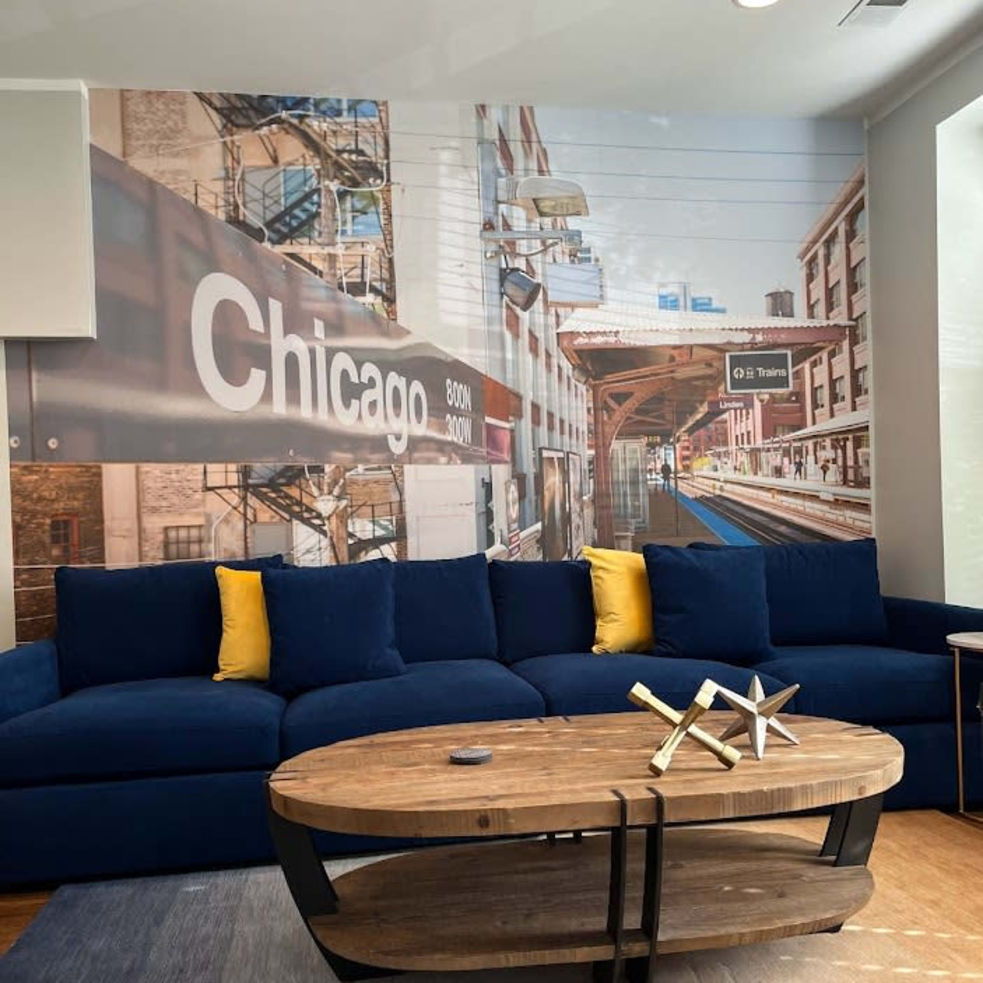 A living room with a blue sectional sofa, a wooden coffee table, and a mural of a Chicago train station on the wall behind it.