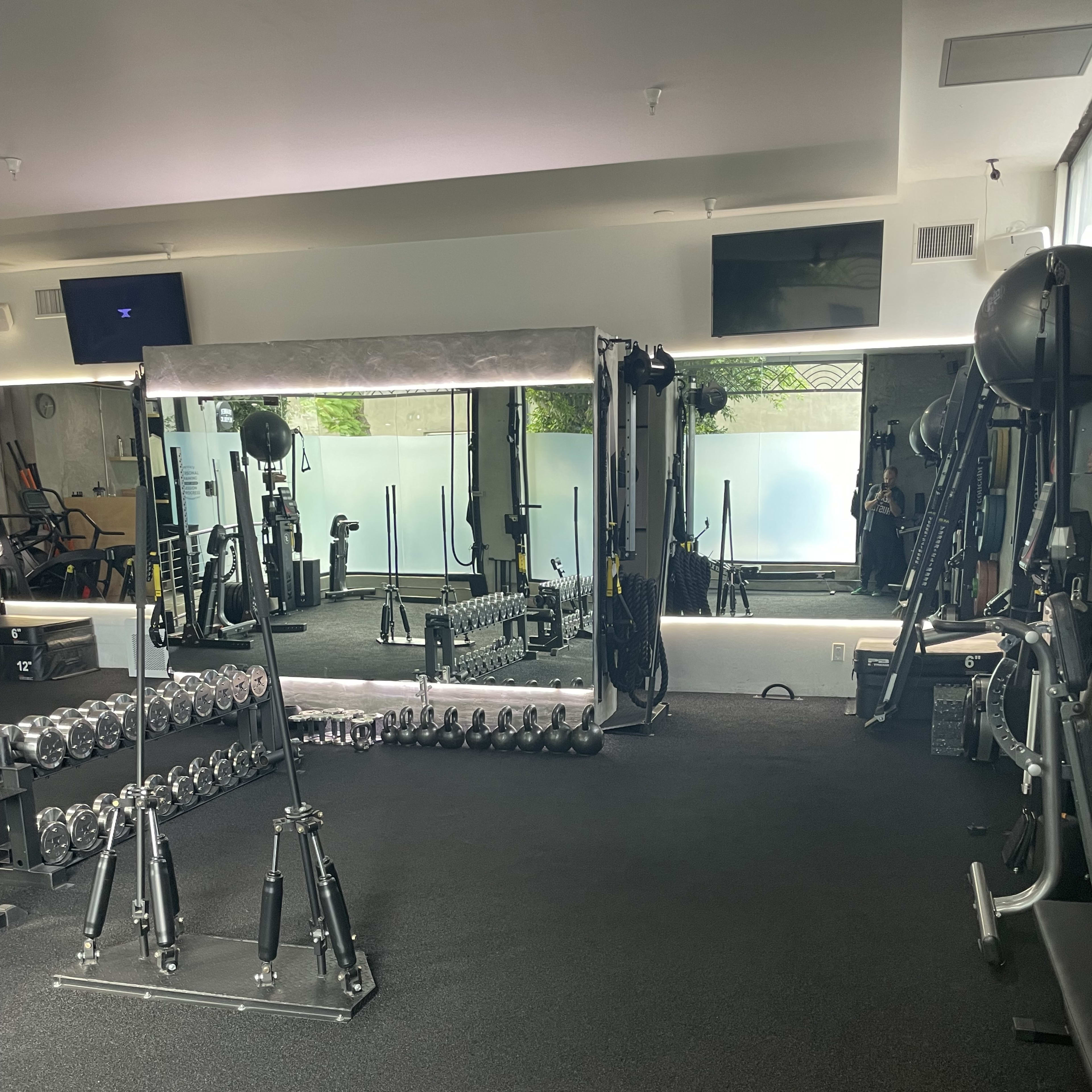 A fitness studio with various gym equipment, including dumbbells arranged in a rack and a large mirror across from a workout area.