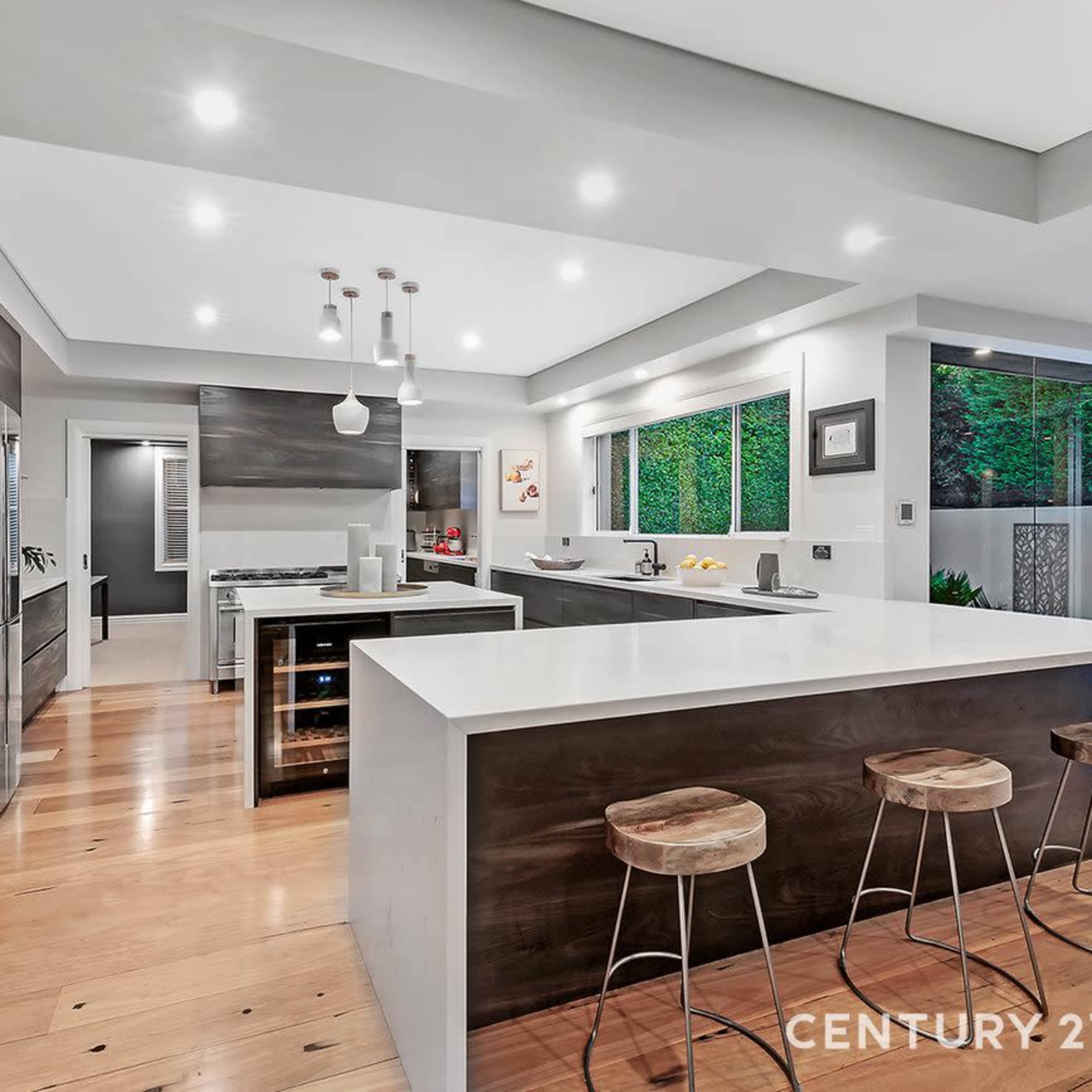 A modern kitchen featuring a large island, wooden flooring, and ample natural light from large windows.