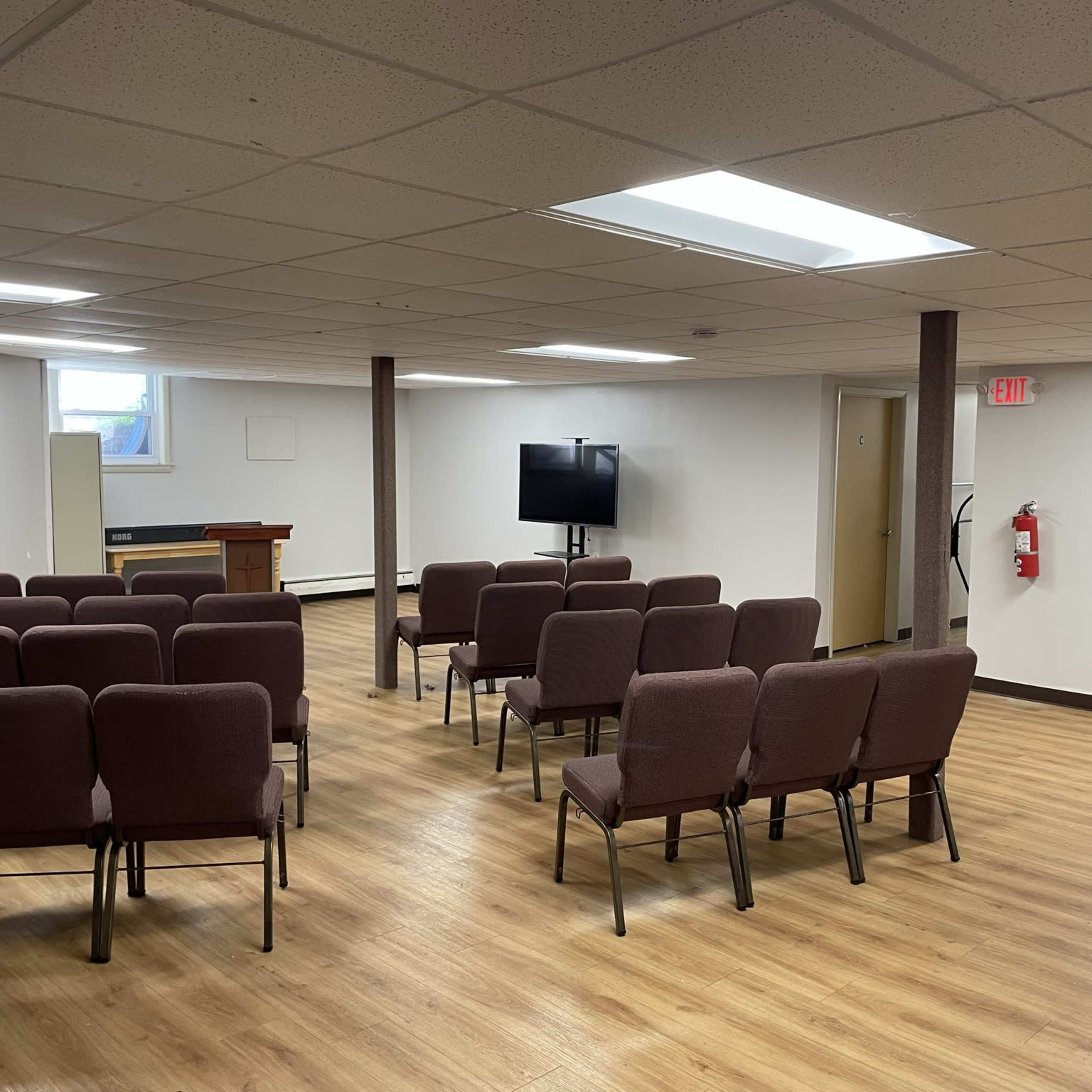 A seating area with several maroon chairs arranged in rows facing a television in a well-lit room with wooden flooring.