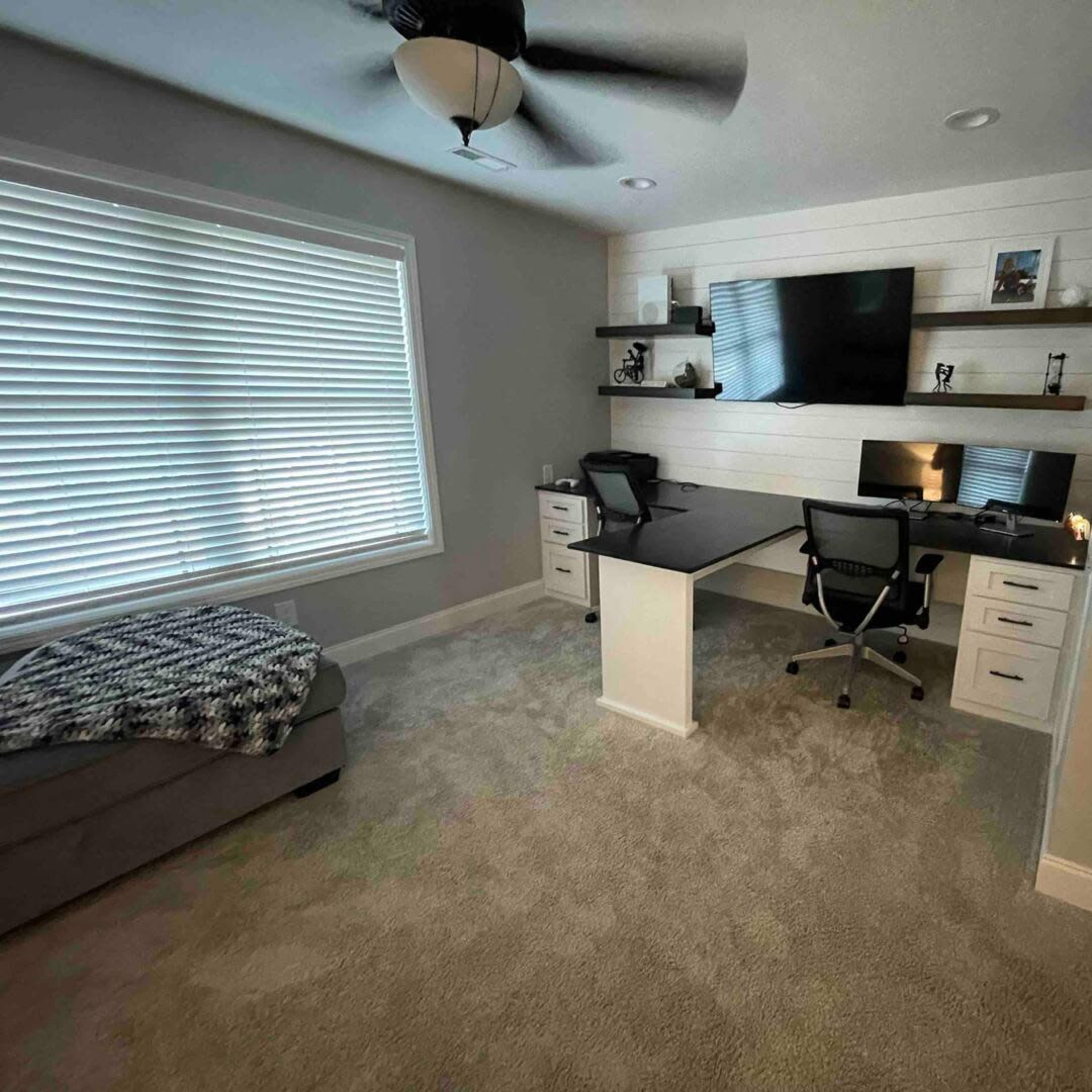 A well-organized home office with two chairs and a large desk against a wall featuring shelving and a mounted TV.