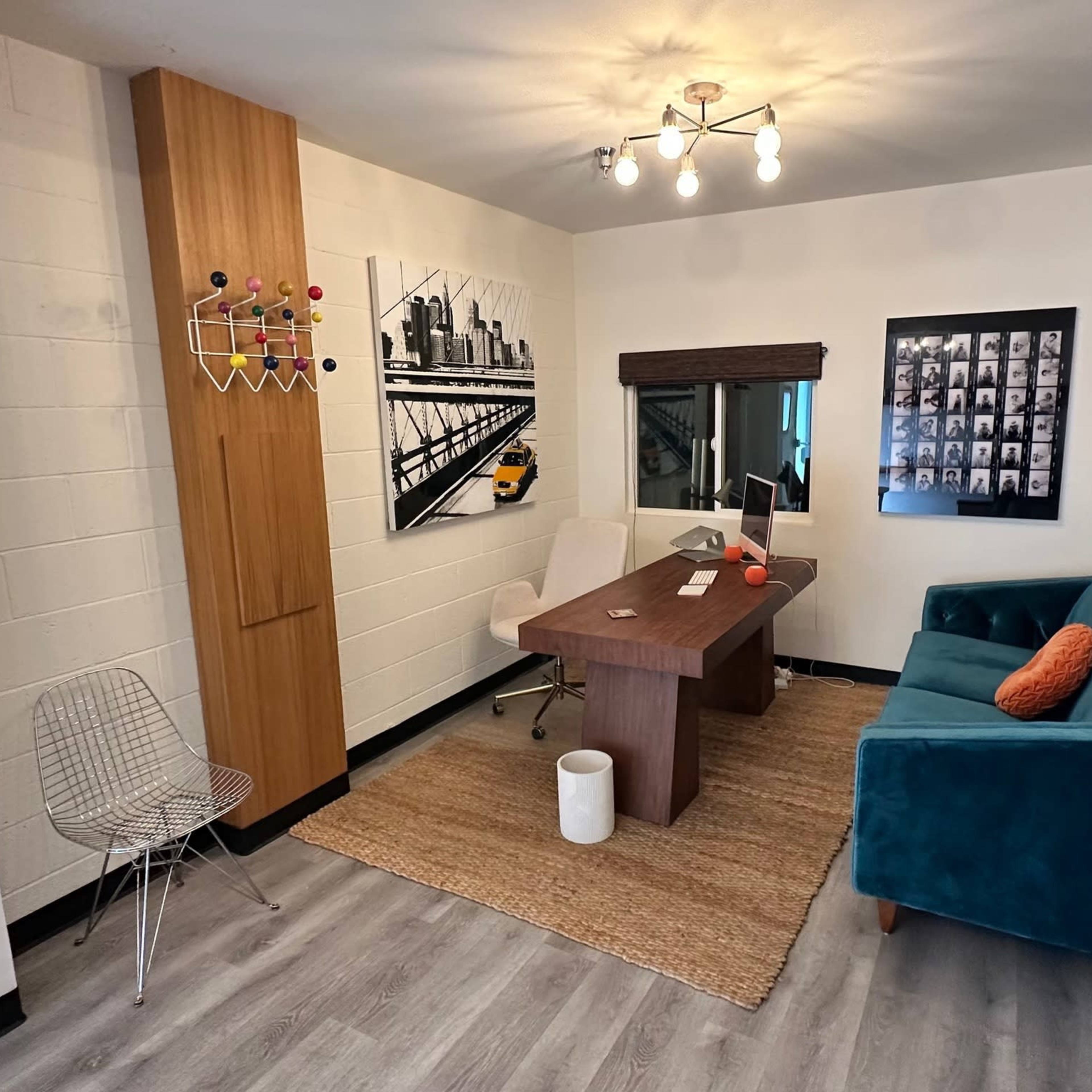 A modern office space with a wooden desk, a teal couch, and decorative wall art.
