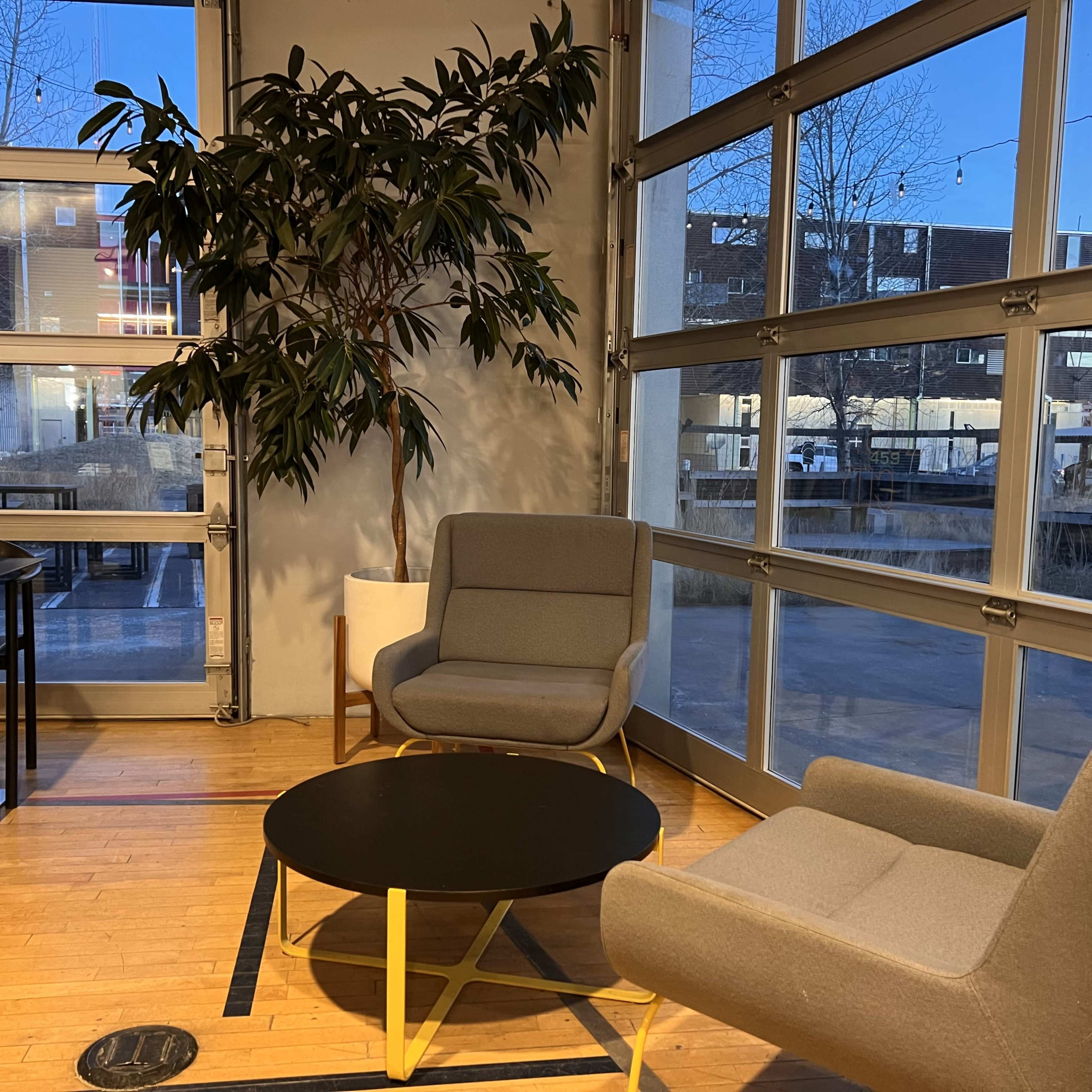 The scene shows a cozy seating area with two gray chairs and a black coffee table beside a large window, revealing a nighttime outdoor view.