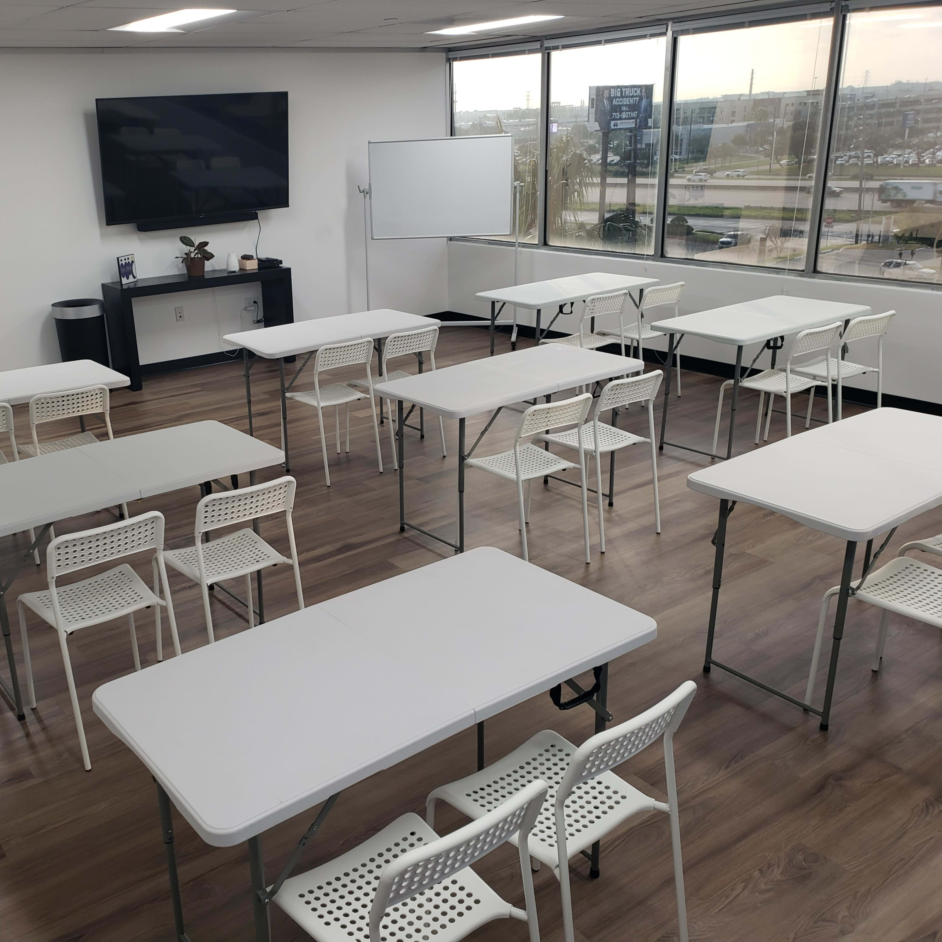 A modern classroom with multiple rows of white tables and chairs arranged in a spacious, well-lit area.