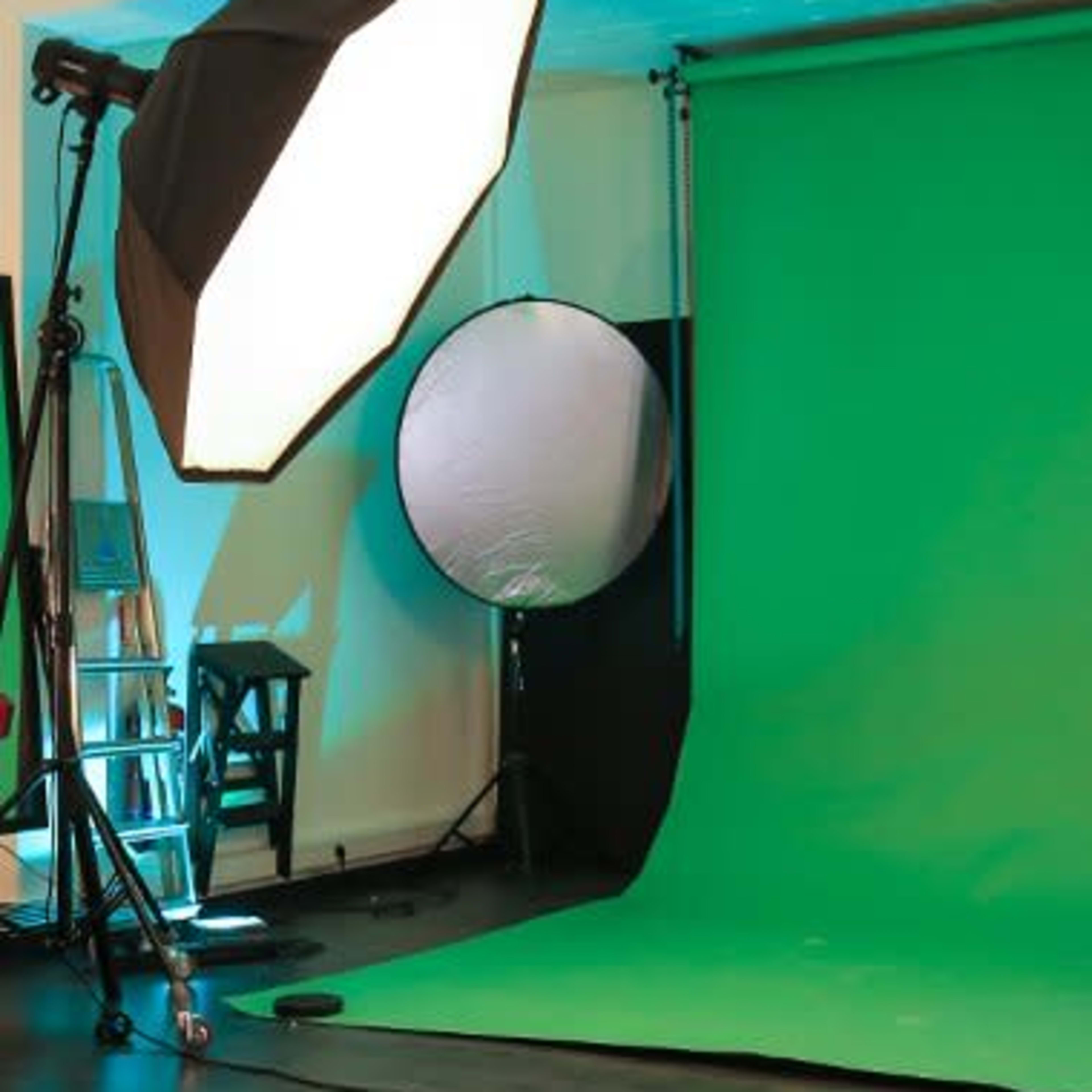 A photography studio setup featuring a green backdrop, a large softbox light, and a reflective disc.