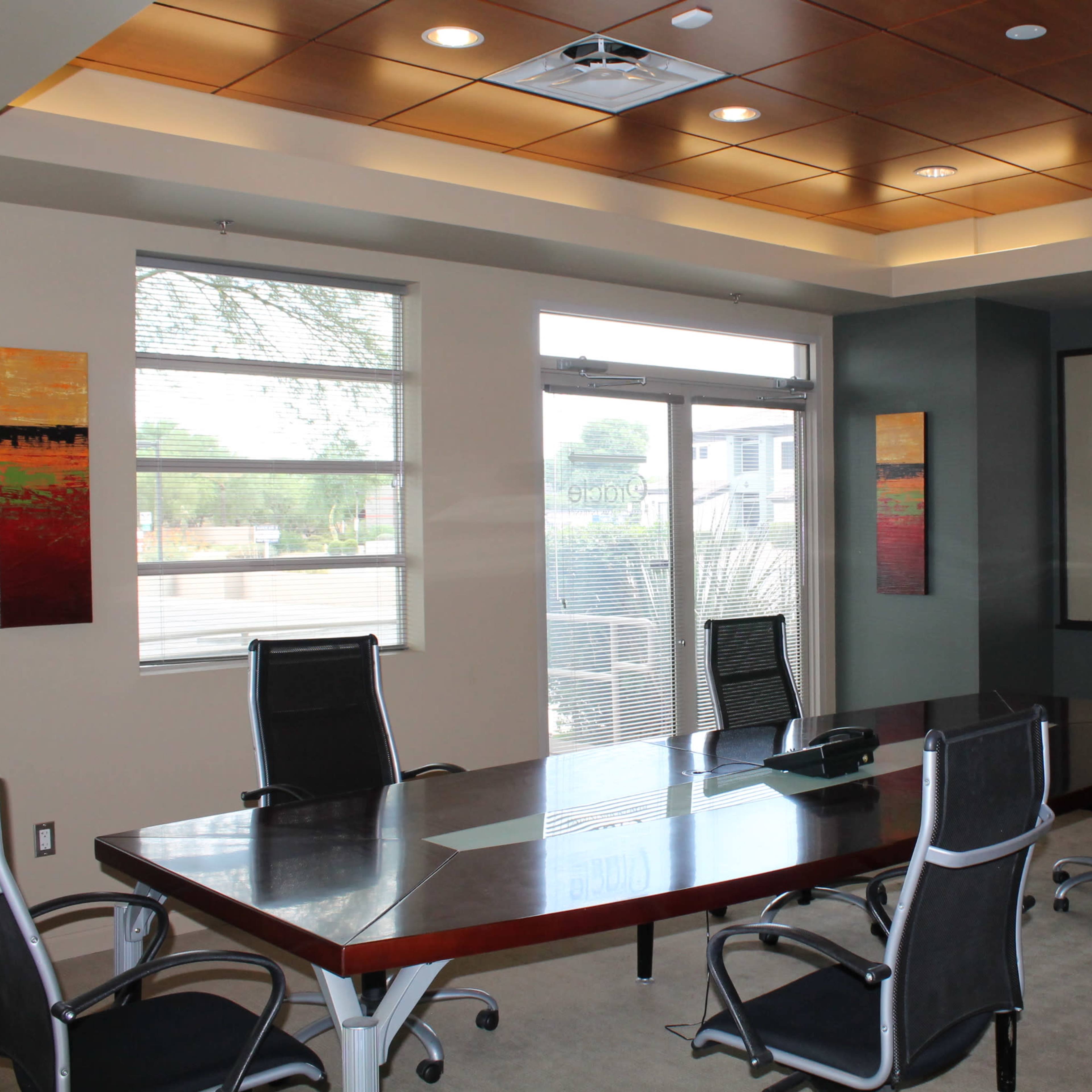 A conference room features a large rectangular table surrounded by six ergonomic chairs, with windows and a whiteboard on the walls.