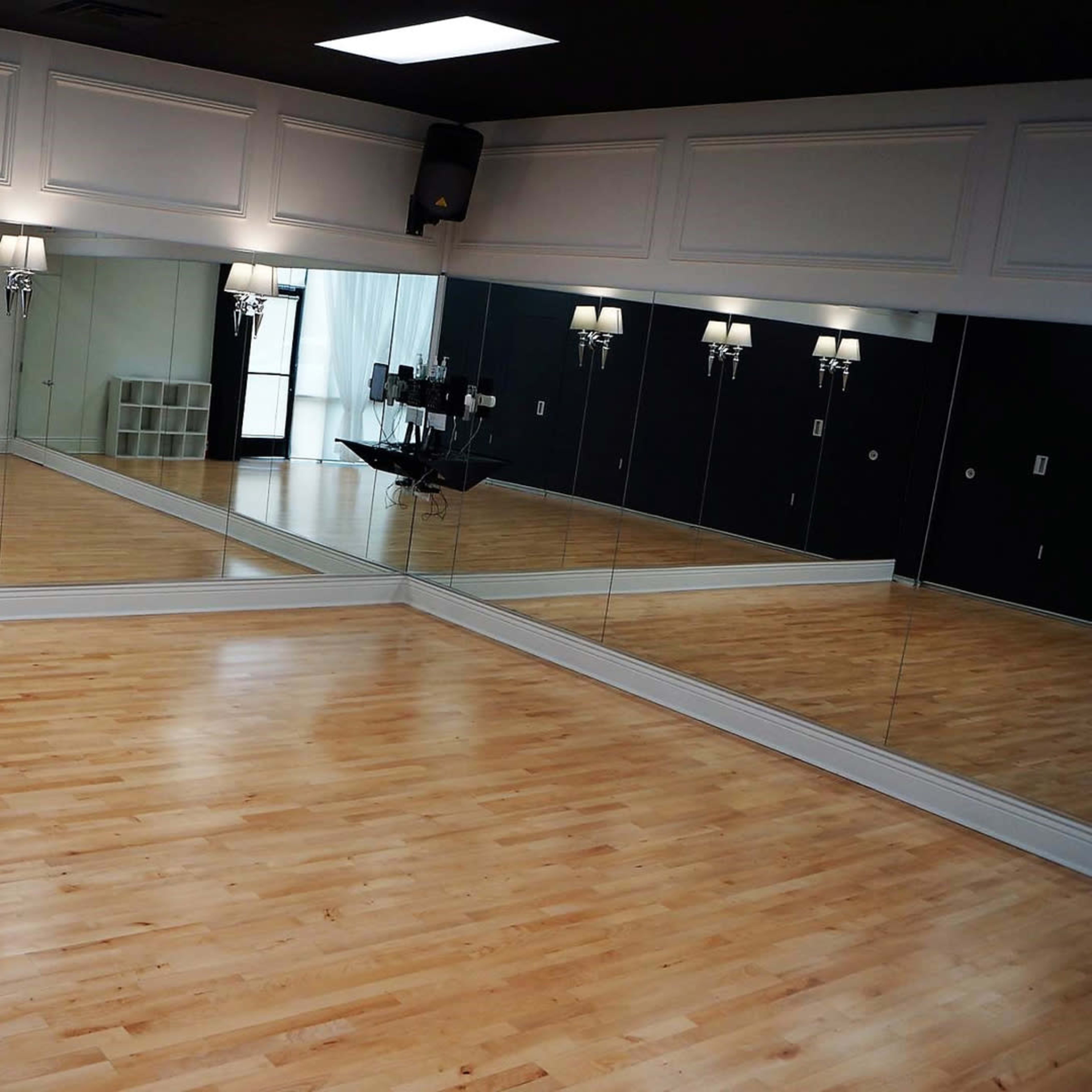 An empty dance studio with mirrored walls and polished wooden floors, illuminated by wall sconces and large windows.