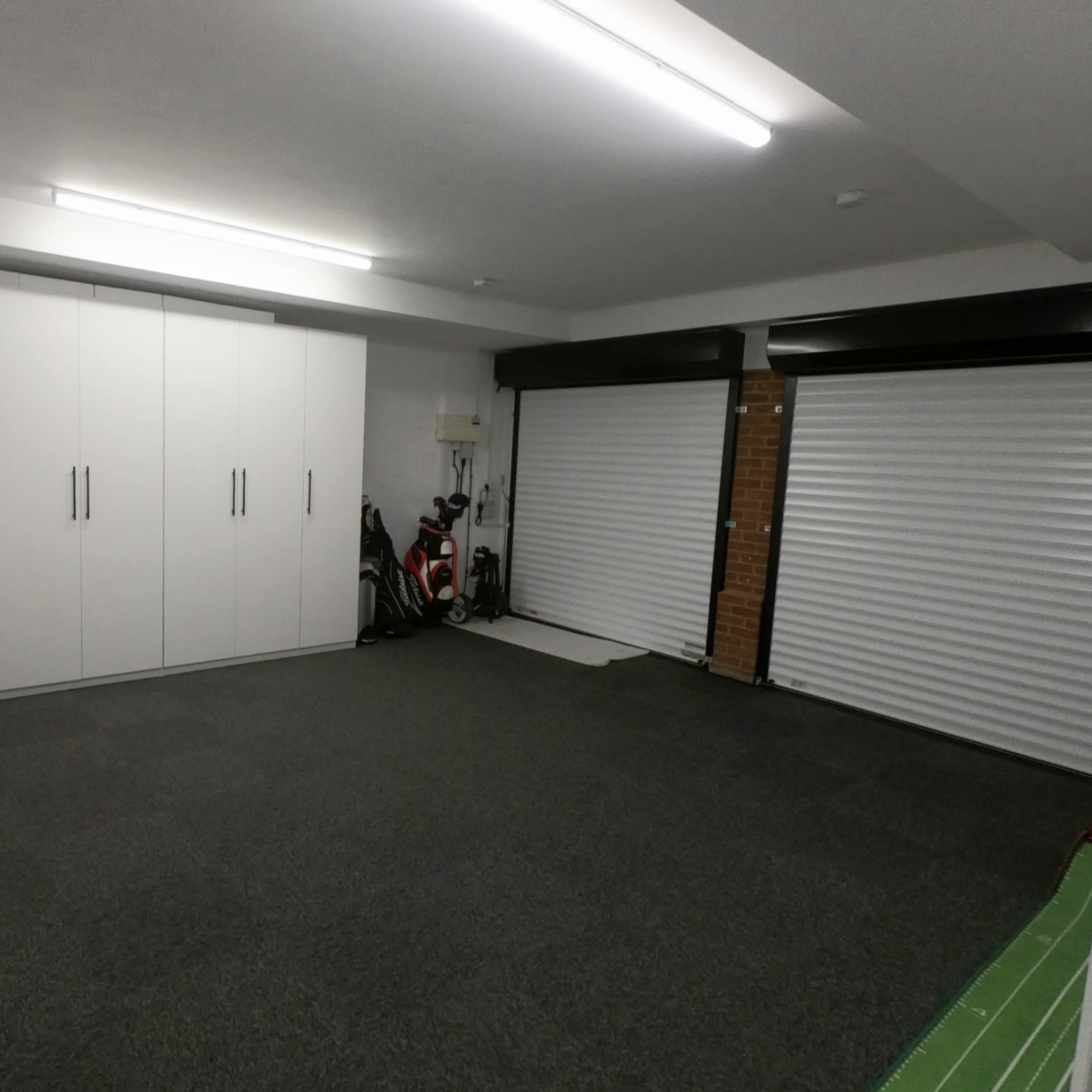 A spacious garage with white cabinets along one wall, two roller doors, and a carpeted floor.