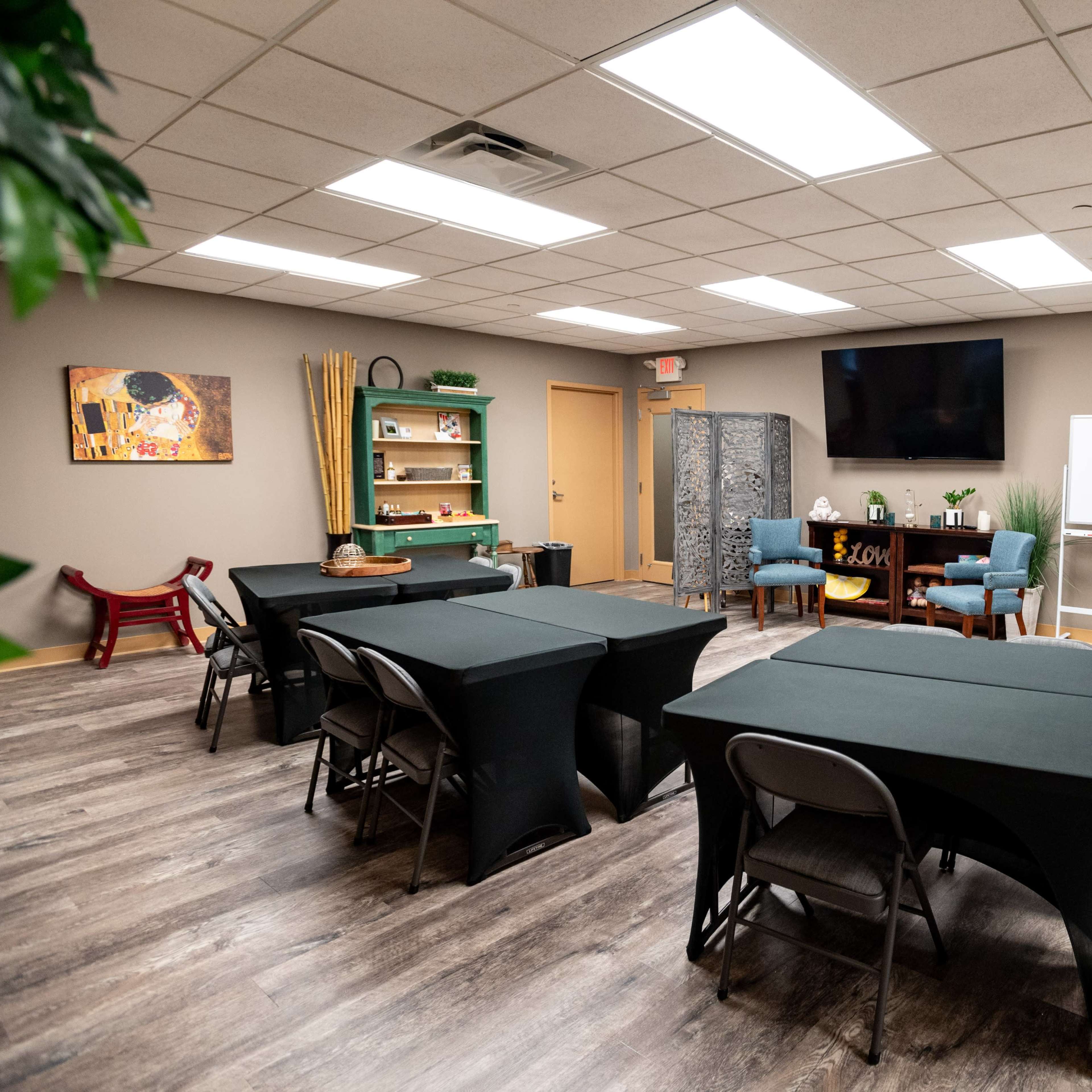 A modern training room is arranged with several black tables and chairs, featuring a TV, a whiteboard, and decoration along the walls.