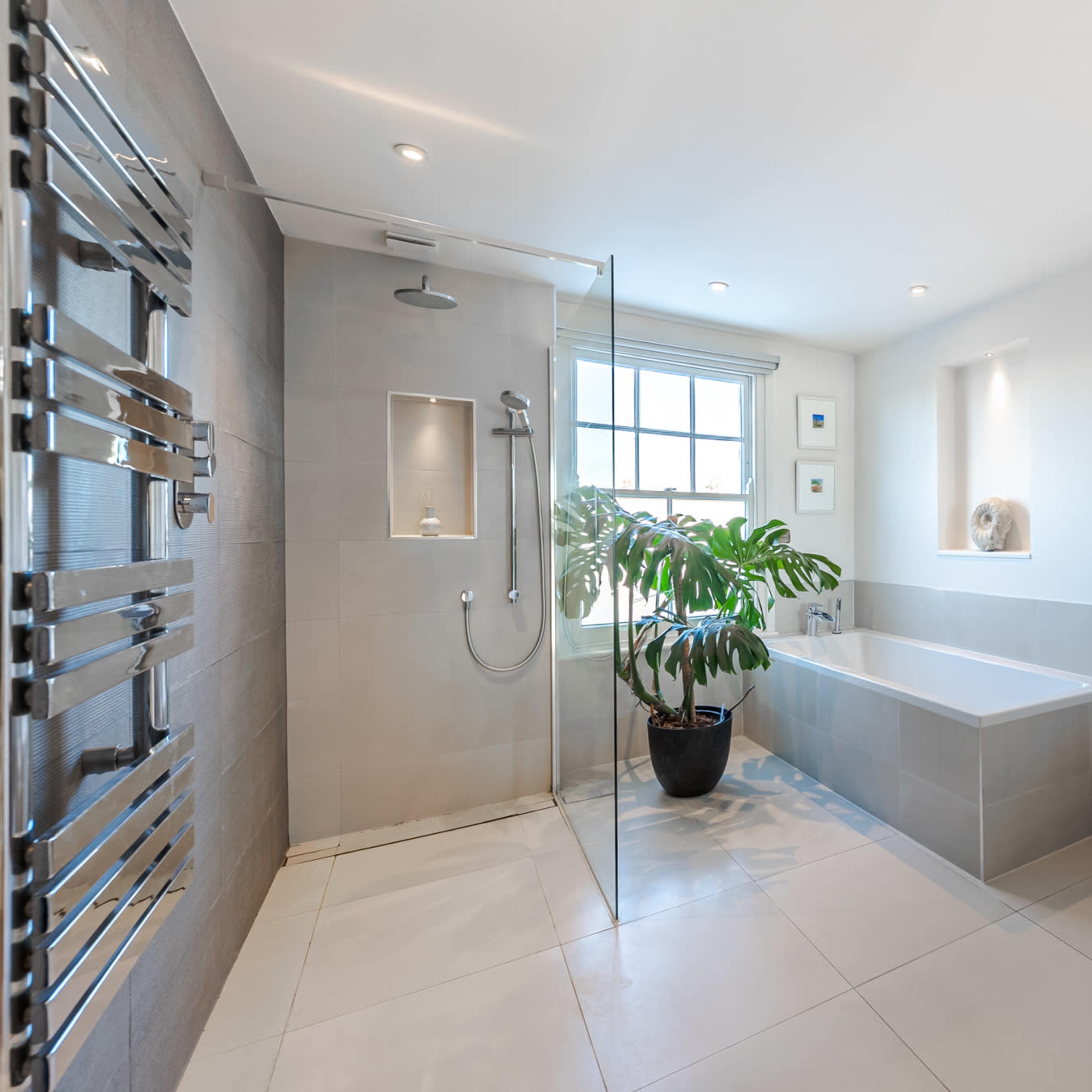 A modern bathroom featuring a glass shower, a freestanding bathtub, a wall-mounted toilet, and a large window with natural light.