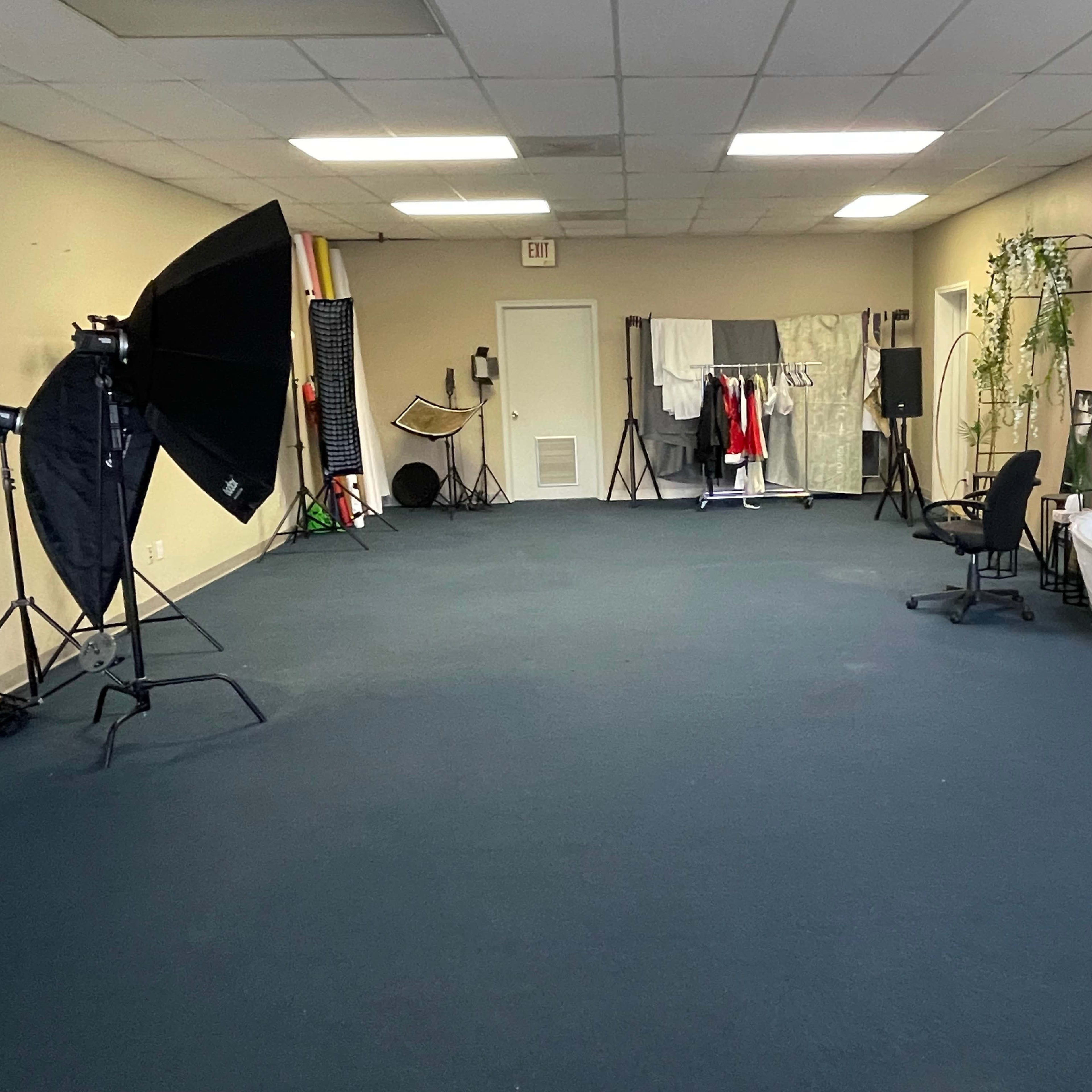 A spacious room with a blue carpet, equipped with photography lighting, a clothes rack, a chair, and a bathtub.