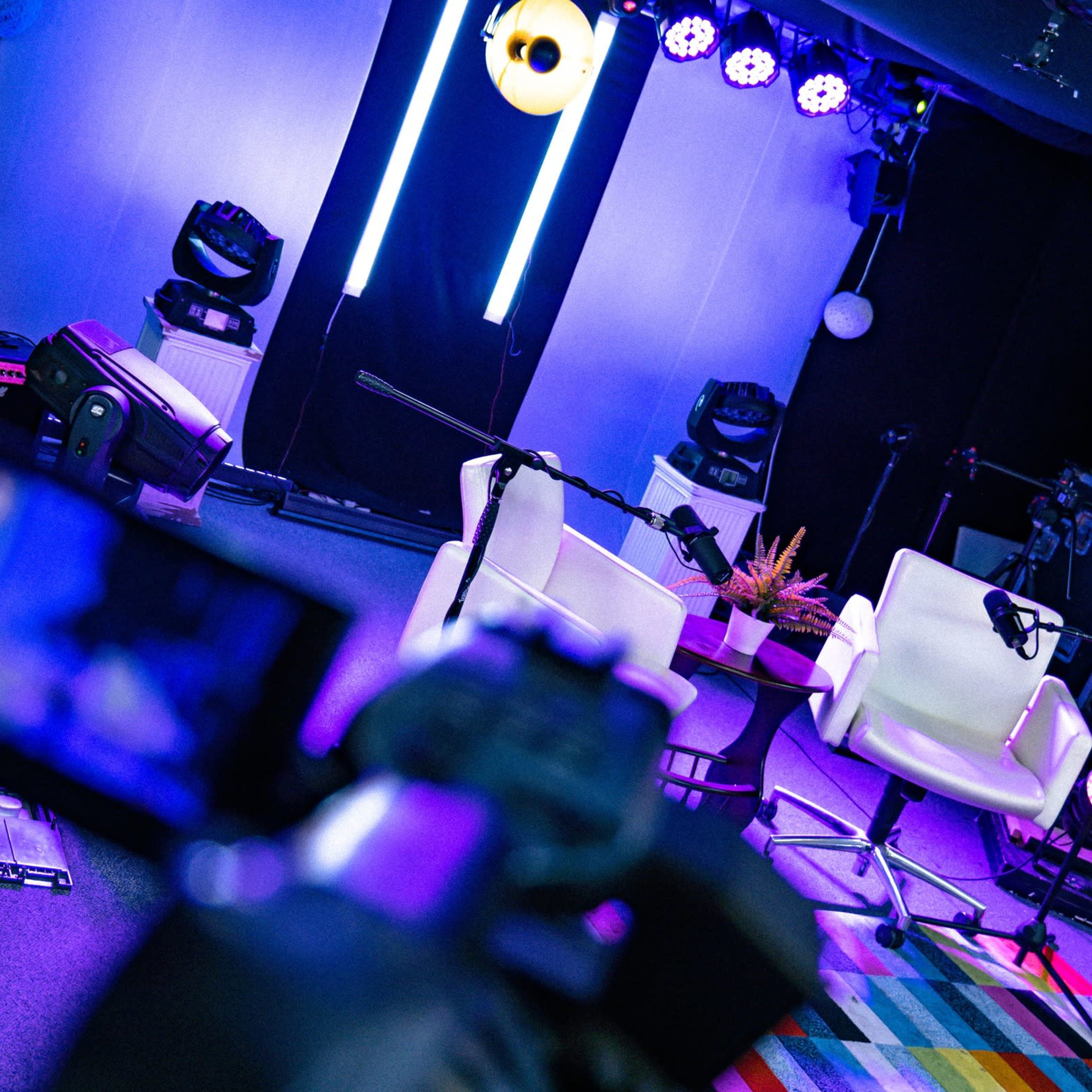 A brightly lit studio setup featuring two white chairs placed in front of sound equipment and colorful striped flooring.