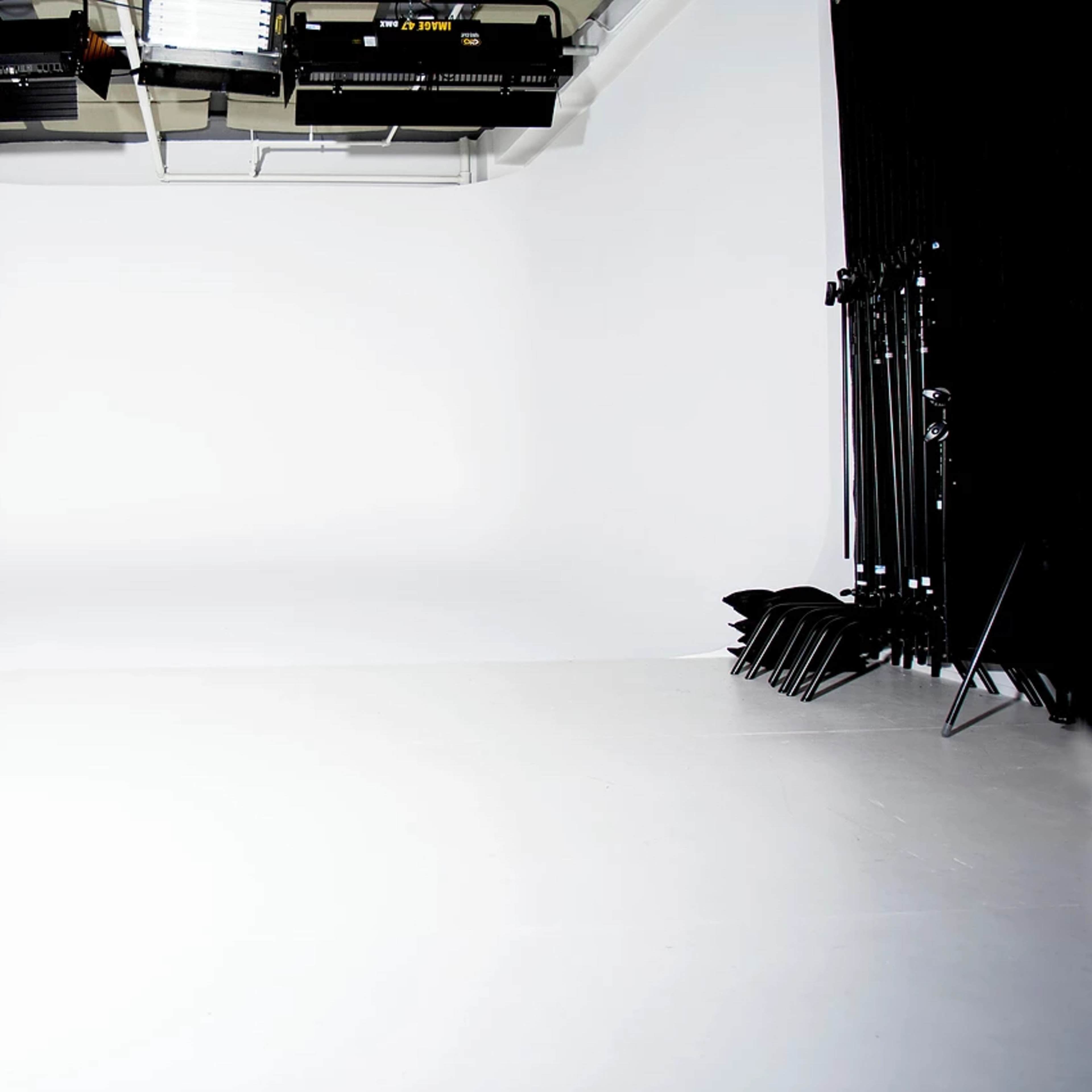 A photo studio with a seamless white backdrop, black curtains, and lighting equipment mounted on the ceiling.