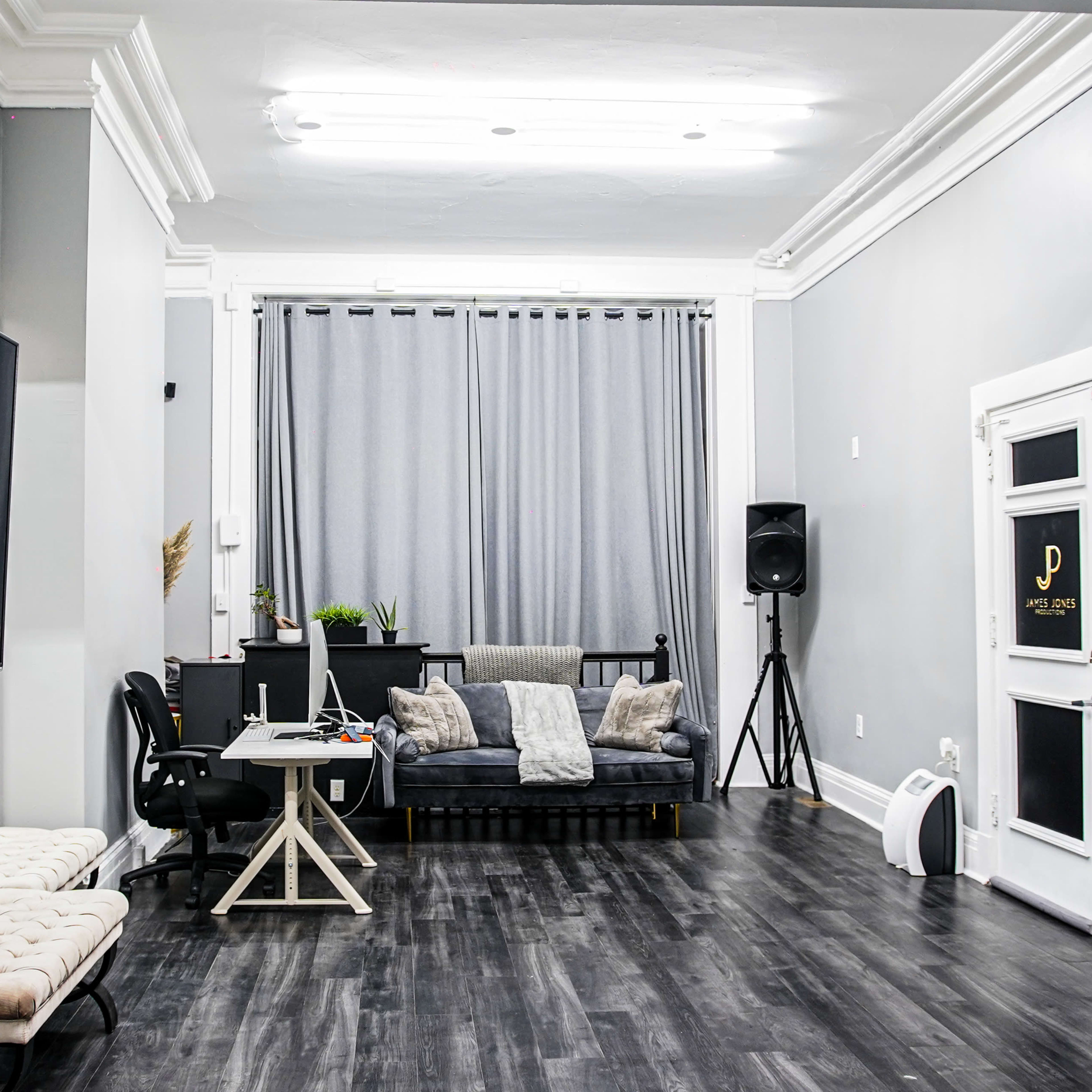 A modern studio features a gray color scheme with a couch, desk, and large screen along one wall.