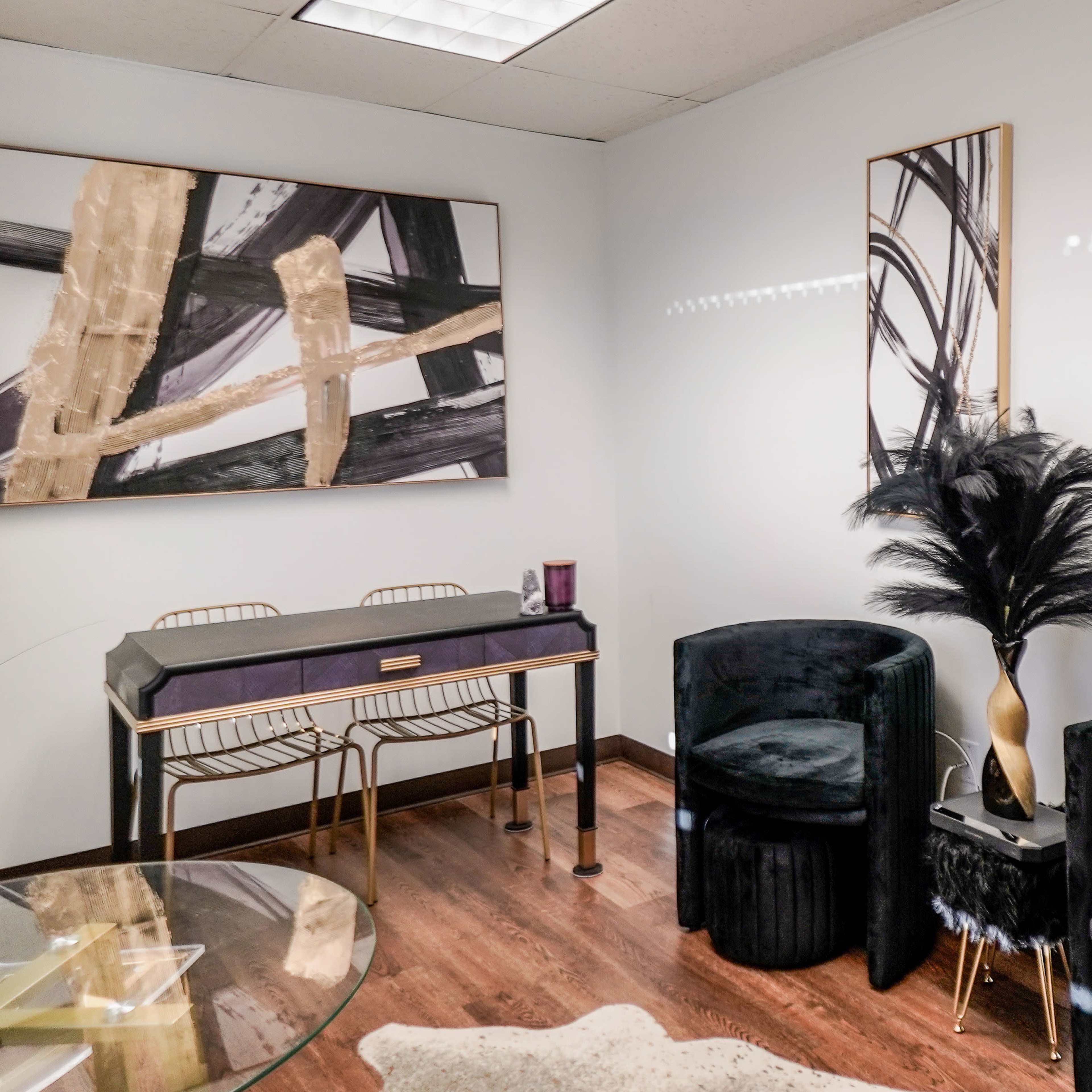 A modern office space with two black upholstered chairs, a small gold desk, and abstract art on the walls.