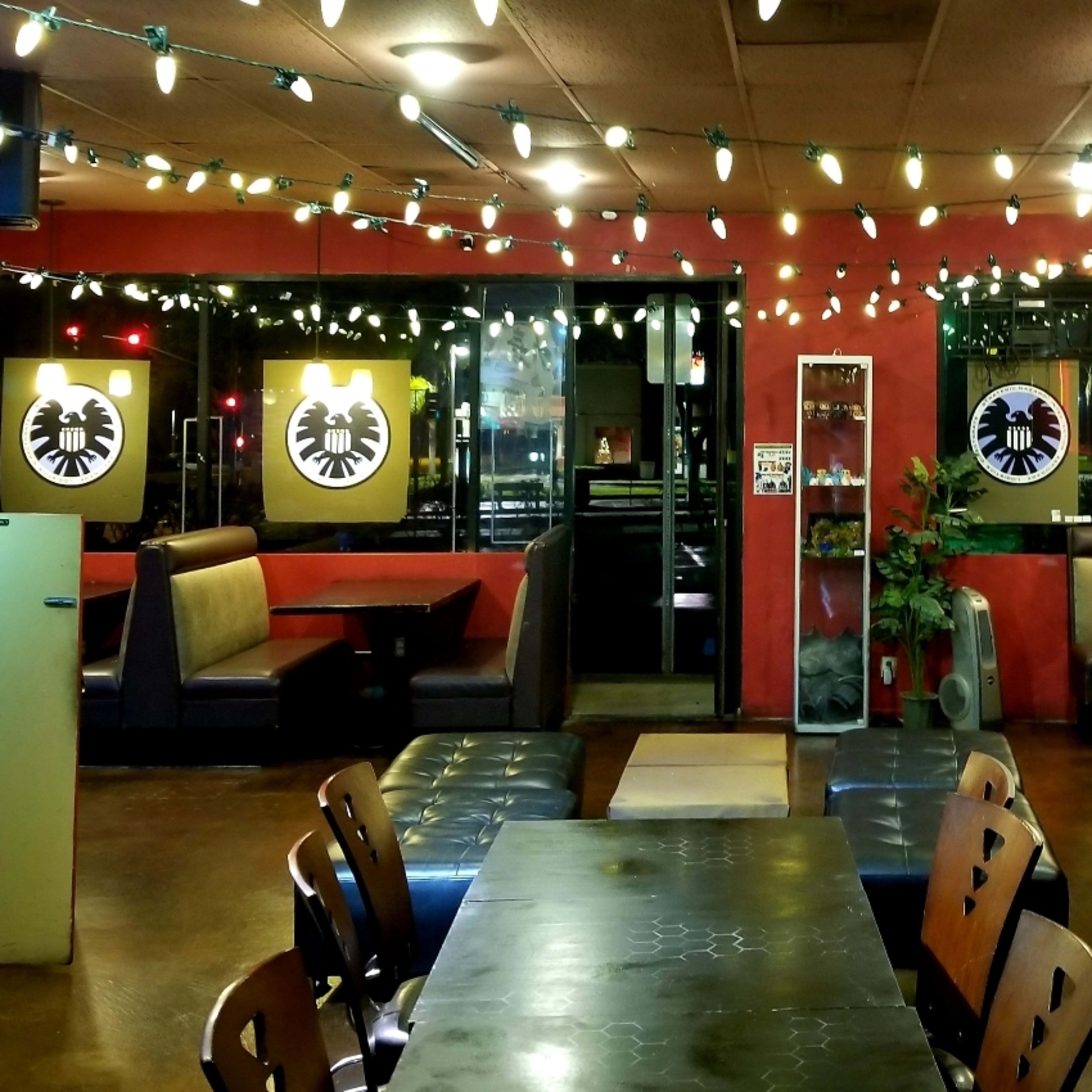 The interior of a restaurant features booths, tables, and wall decor, illuminated by string lights hanging from the ceiling.