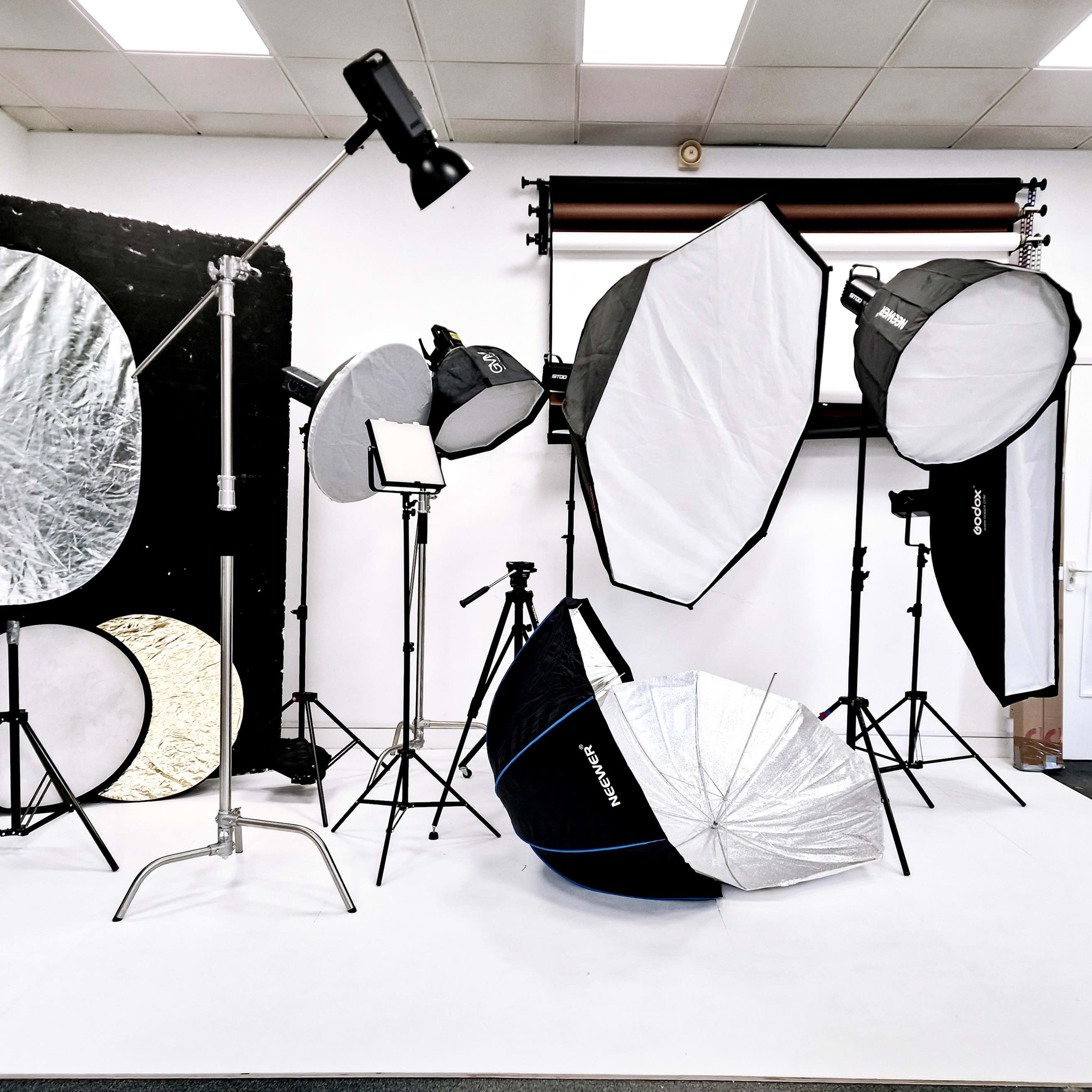 A photography studio is set up with various lighting equipment, including softboxes, reflectors, and light stands arranged on a white backdrop.