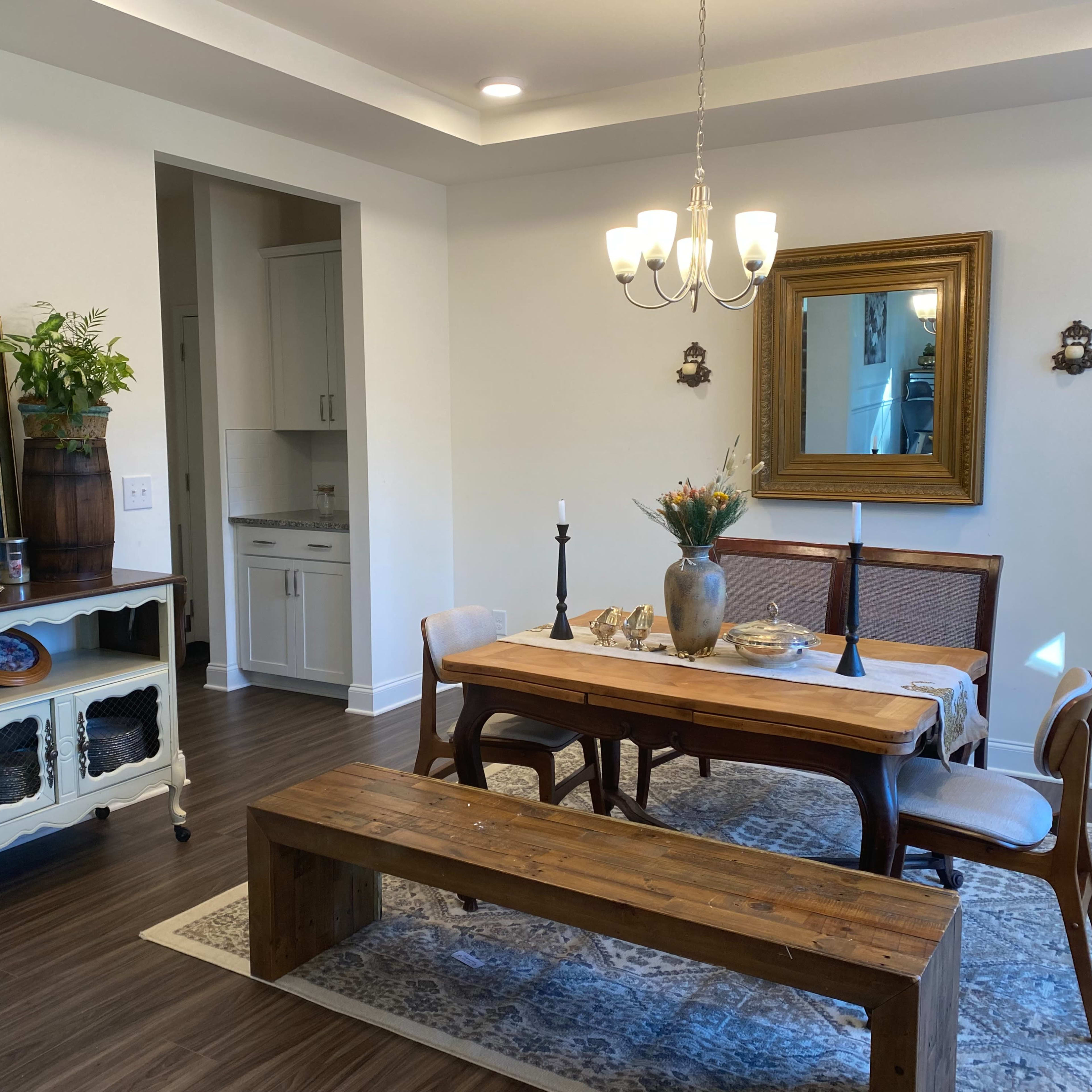 A dining area with a wooden table surrounded by chairs, a sideboard displaying decorative items, and a large mirror reflecting the room's decor.