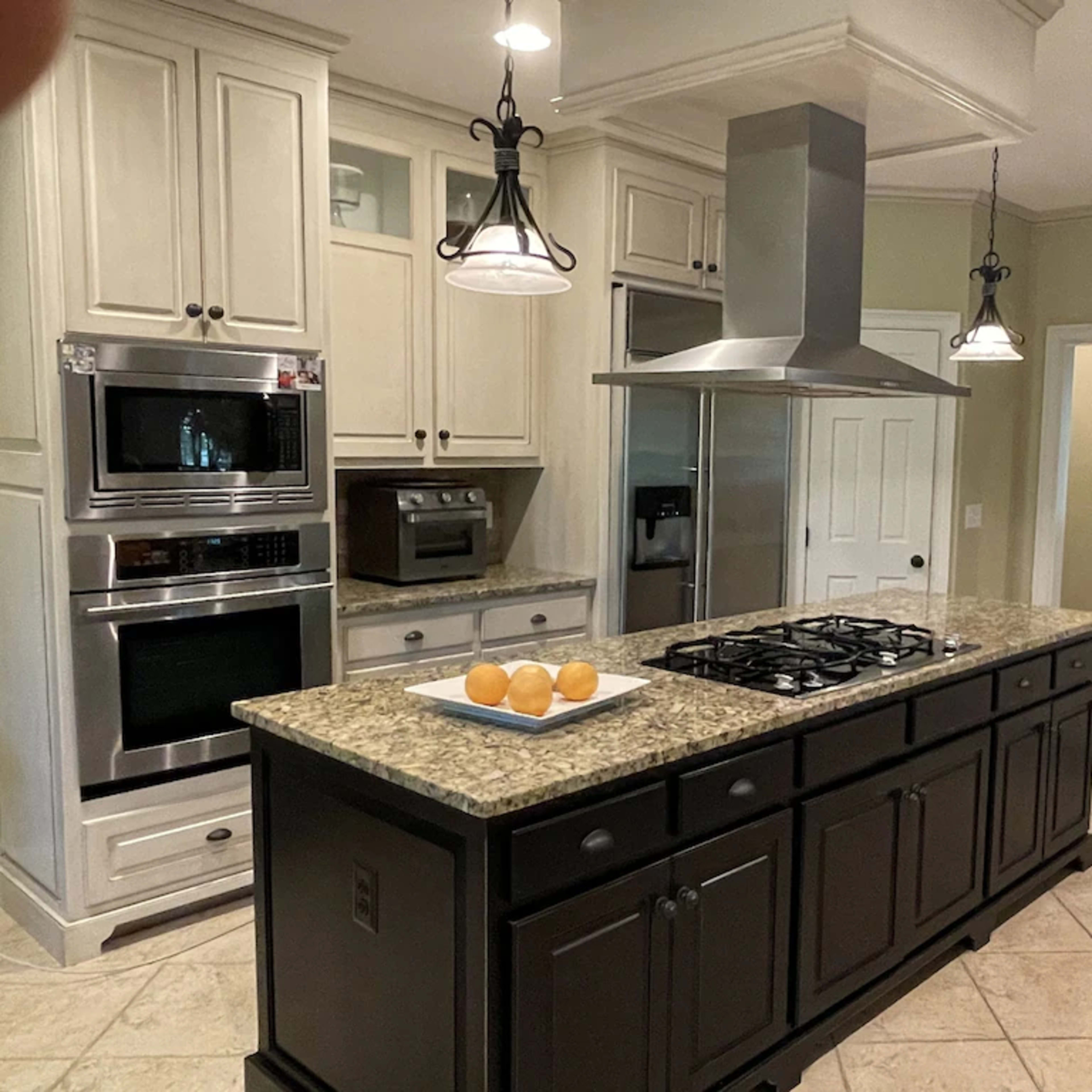 A kitchen features an island with a gas stovetop, flanked by stainless steel appliances and light-colored cabinetry.