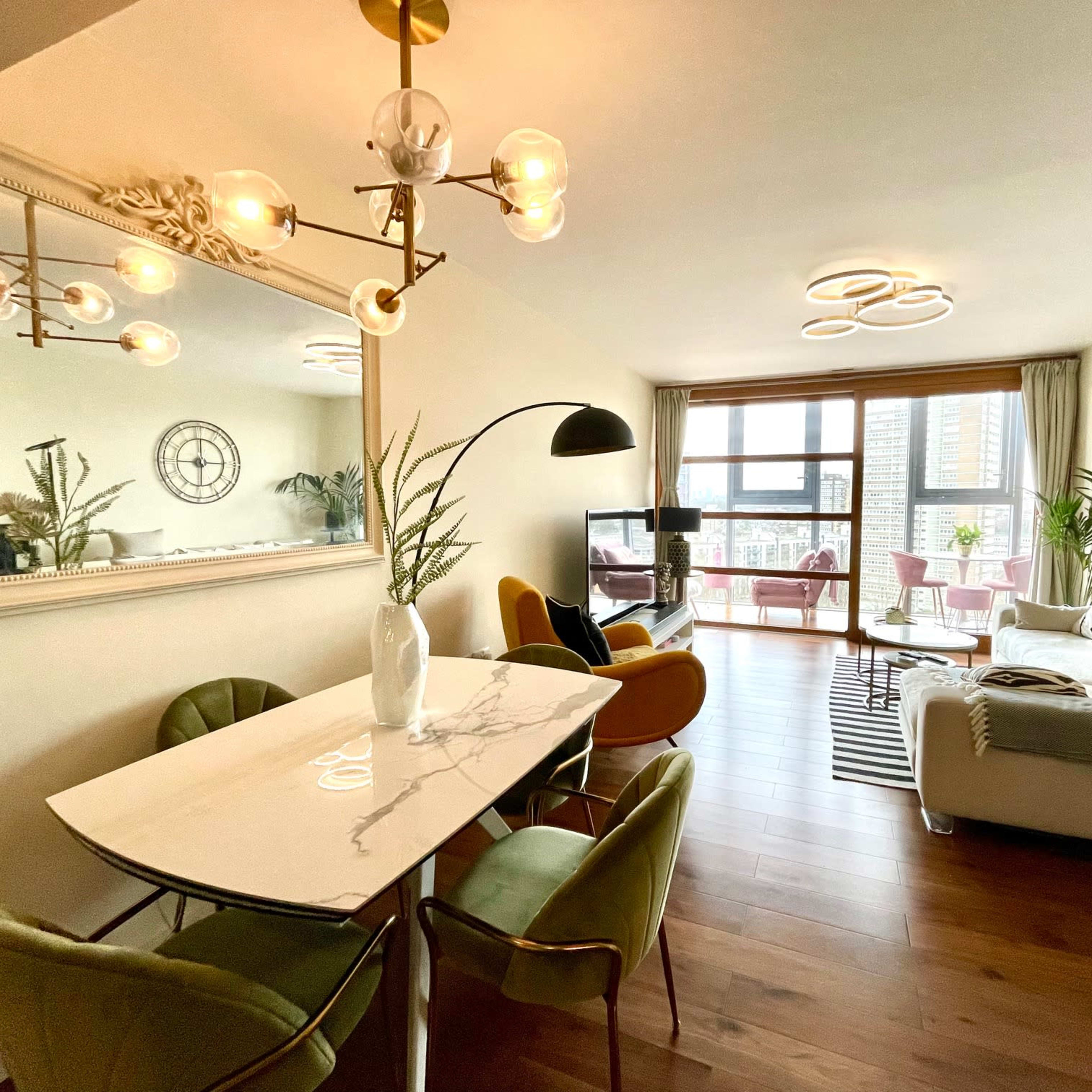 A modern living room and dining area featuring a stylish table, colorful chairs, and large windows with a balcony view.