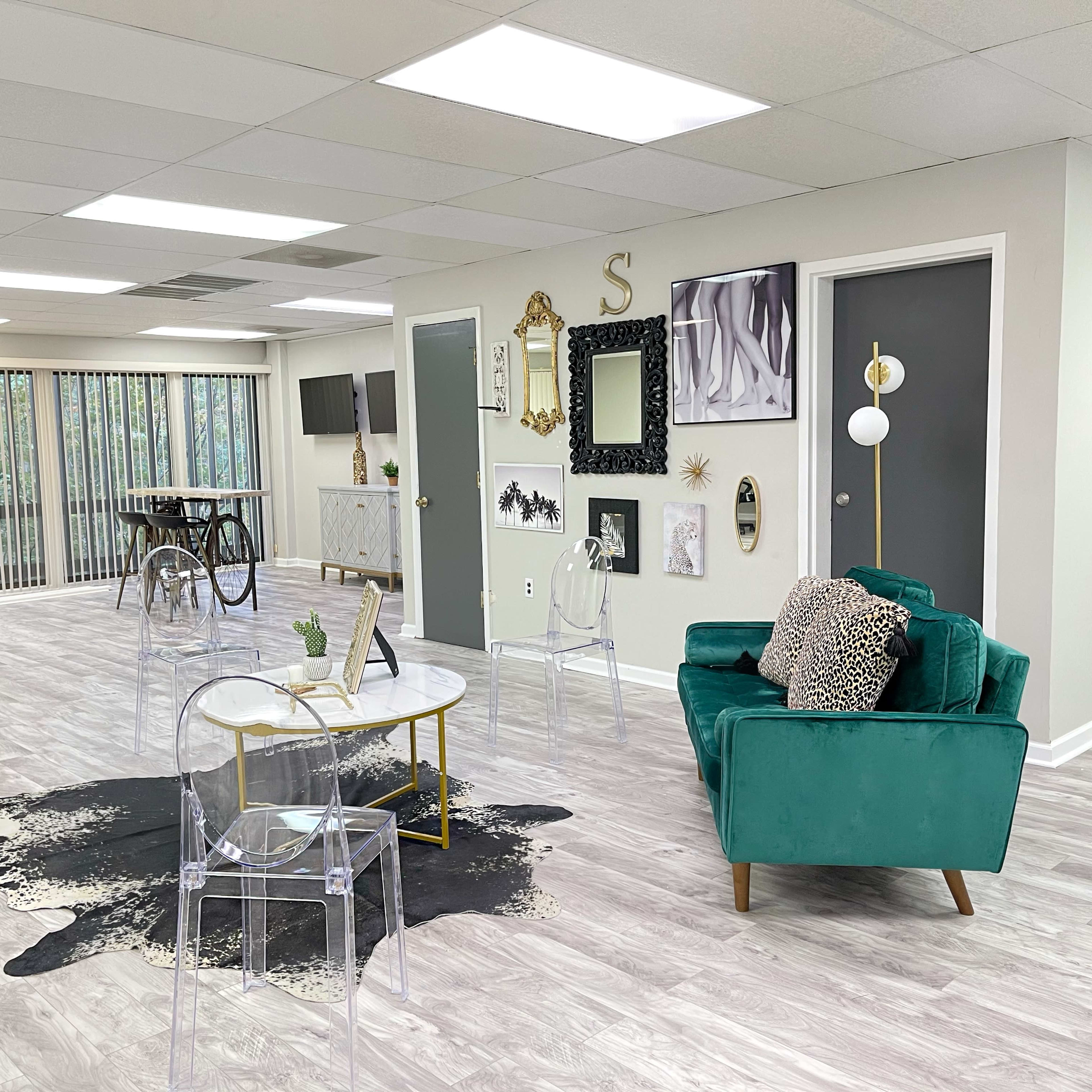 A spacious, modern interior features a green velvet couch, a clear acrylic coffee table, and various artworks displayed on the walls.
