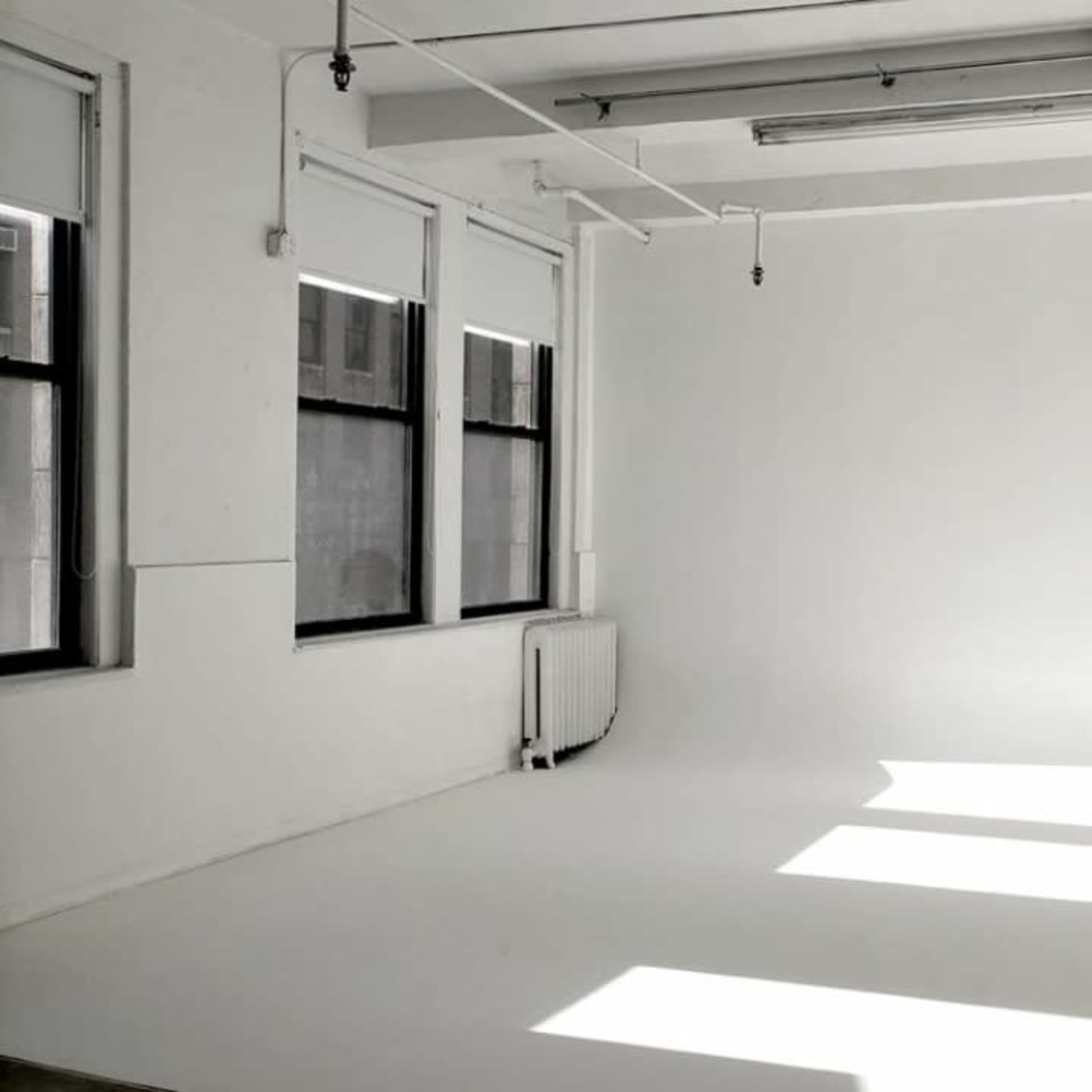 A bright, minimalistic studio space features white walls, a smooth floor, and large windows allowing natural light to stream in.