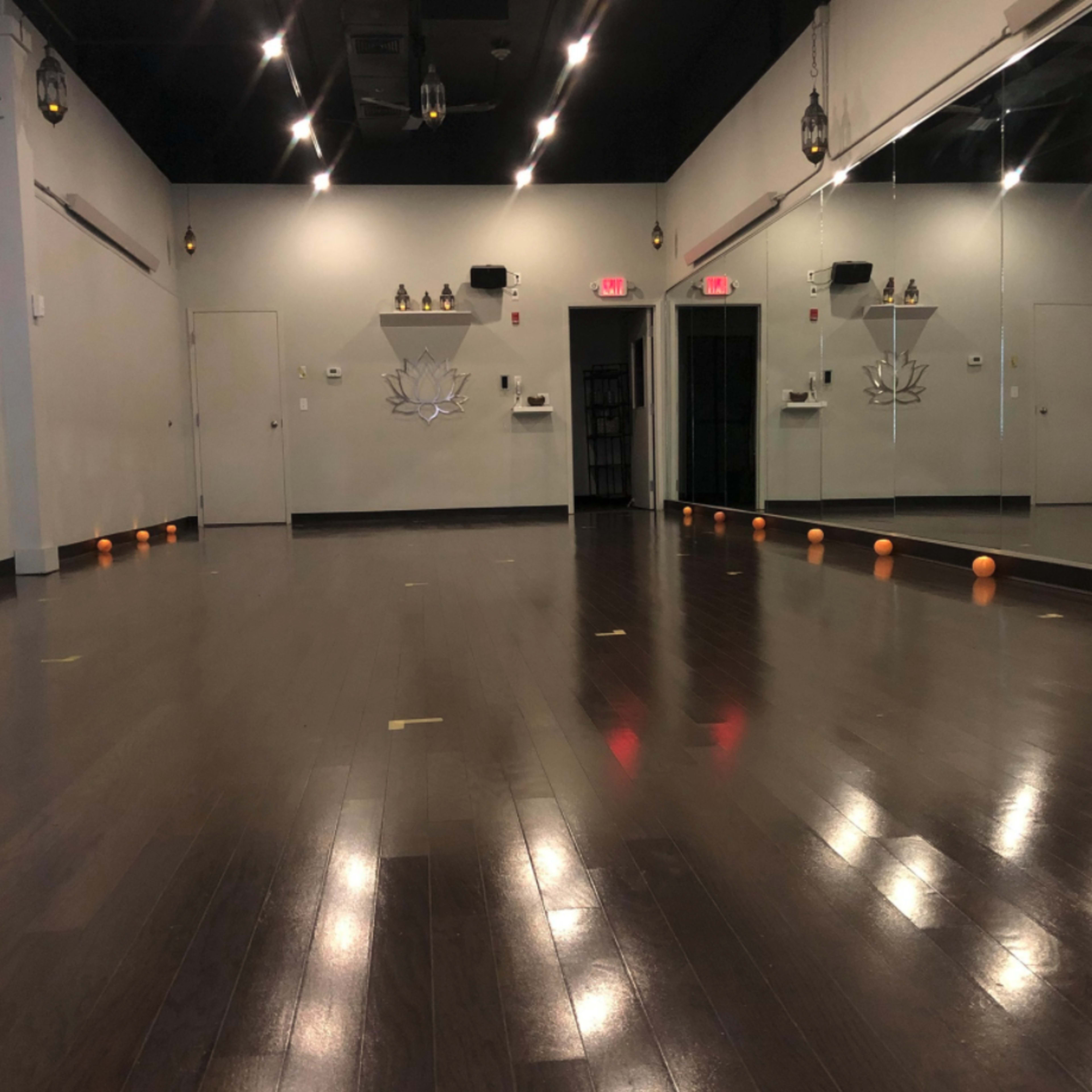 An empty studio with polished wooden floors, mirrors on one wall, and several small orange objects lined up along the floor.