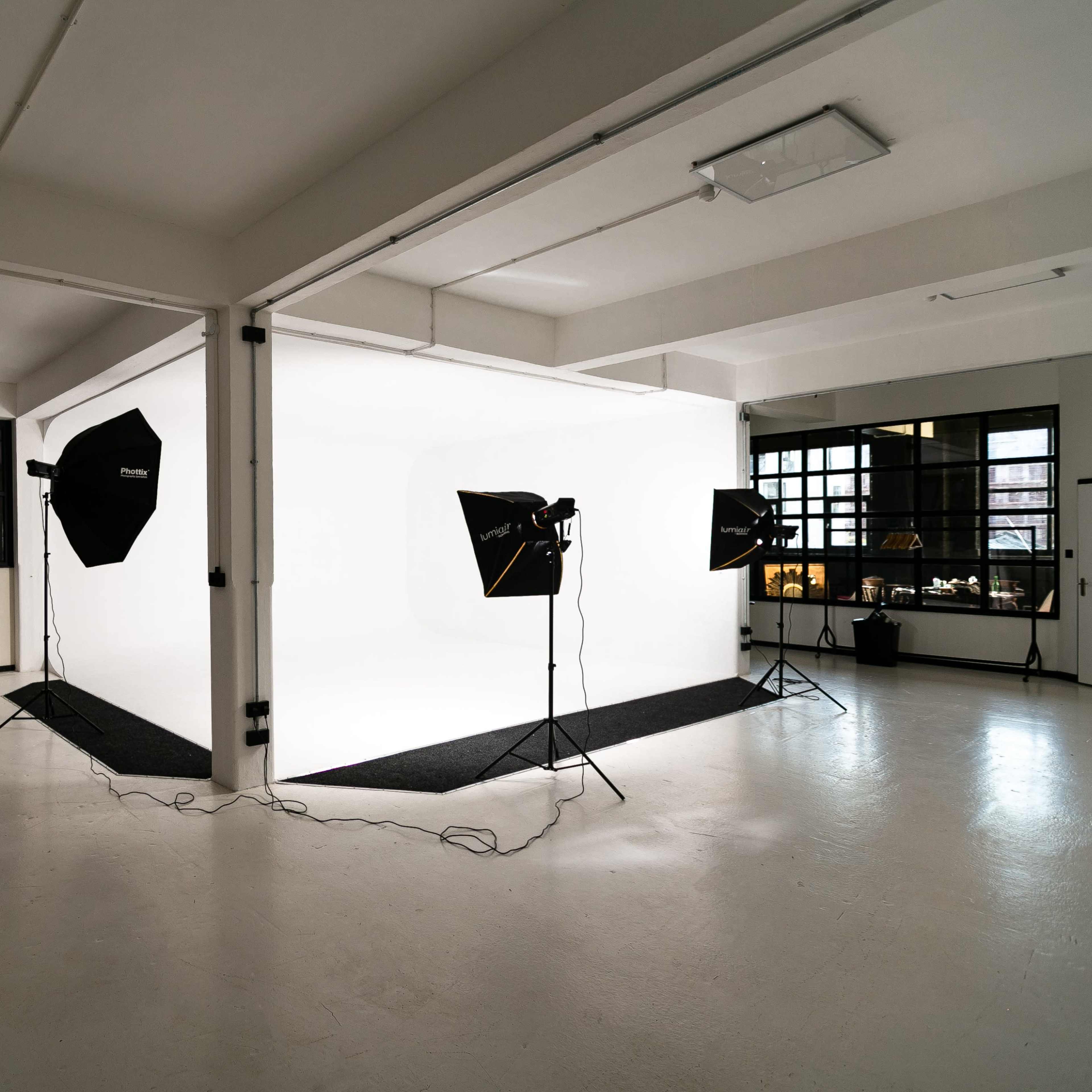 A photography studio features a seamless white backdrop illuminated by several softbox lights and has a minimalist design.
